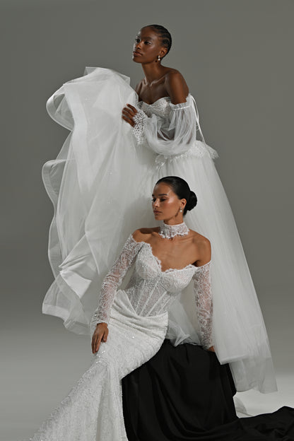 Lace mermaid wedding dress with sweetheart corset and tulle overskirt – two brides seated on a black block