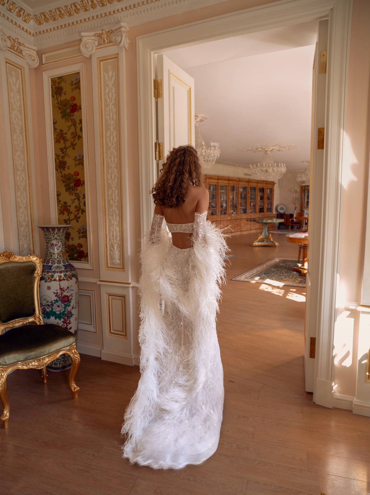 An elegant halter column wedding gown crafted in hand-beaded lace with detachable lace sleeves and a dramatic feather stole. Modern, sculpted, and exquisitely glamorous.