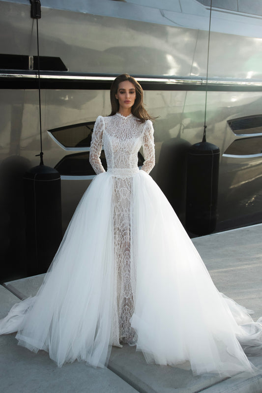 Celeste beaded lace long-sleeve sheath wedding dress with high neck and detachable tulle overskirt, open-back detail.