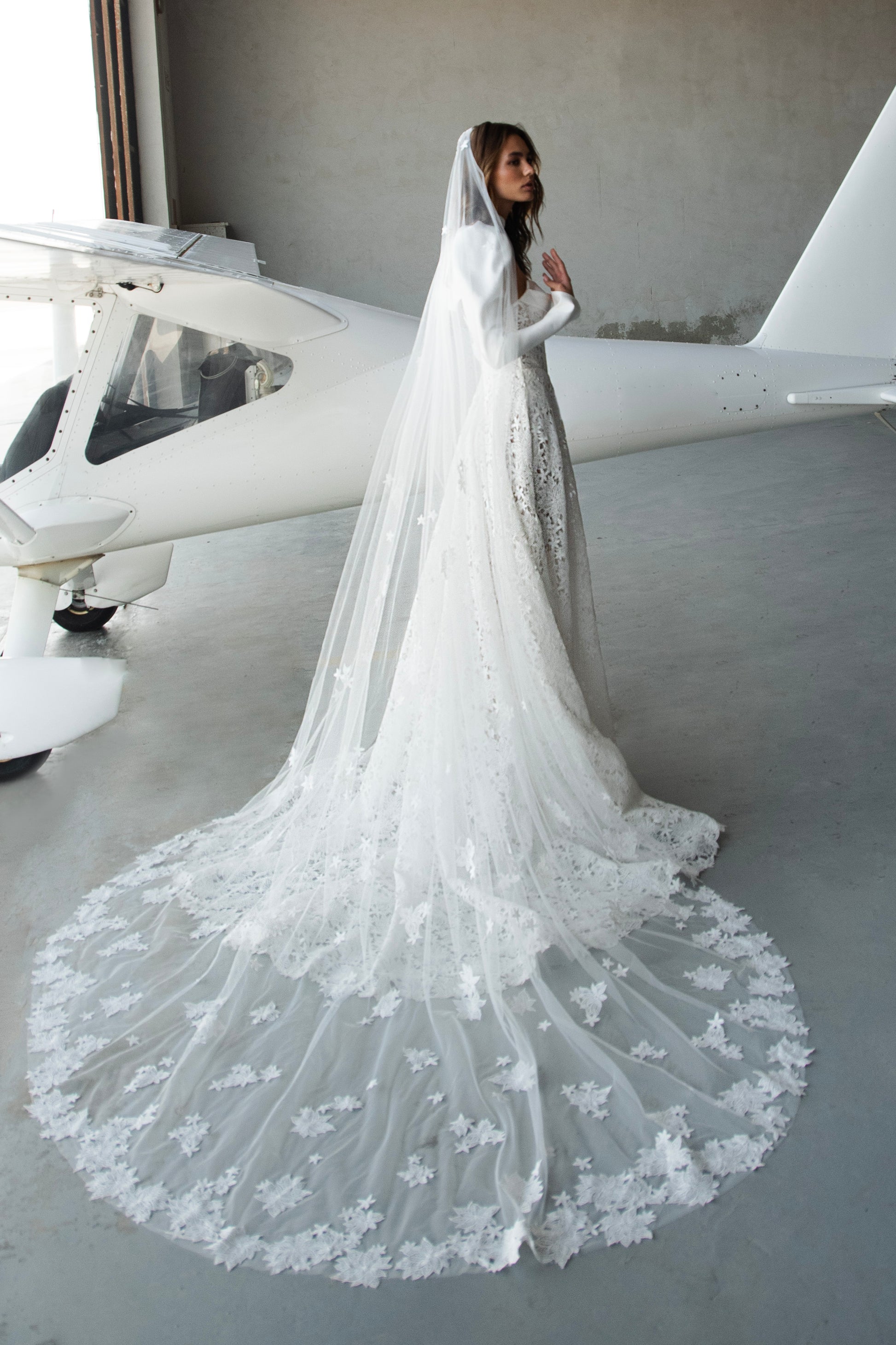 Bride in lace A-line wedding dress with satin bolero, sweetheart corset bodice, long sleeves, and chapel train.