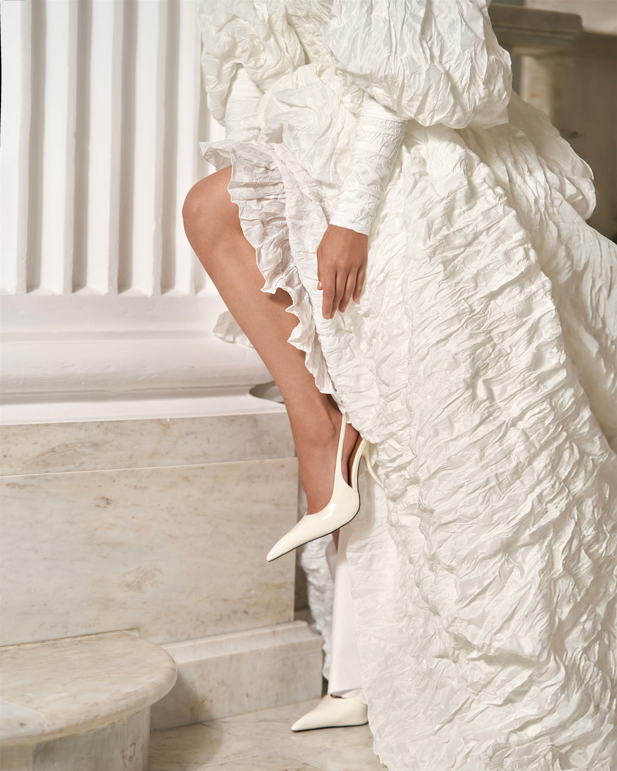 Detail of the open front skirt and sculptural folds of a white textured taffeta wedding dress.