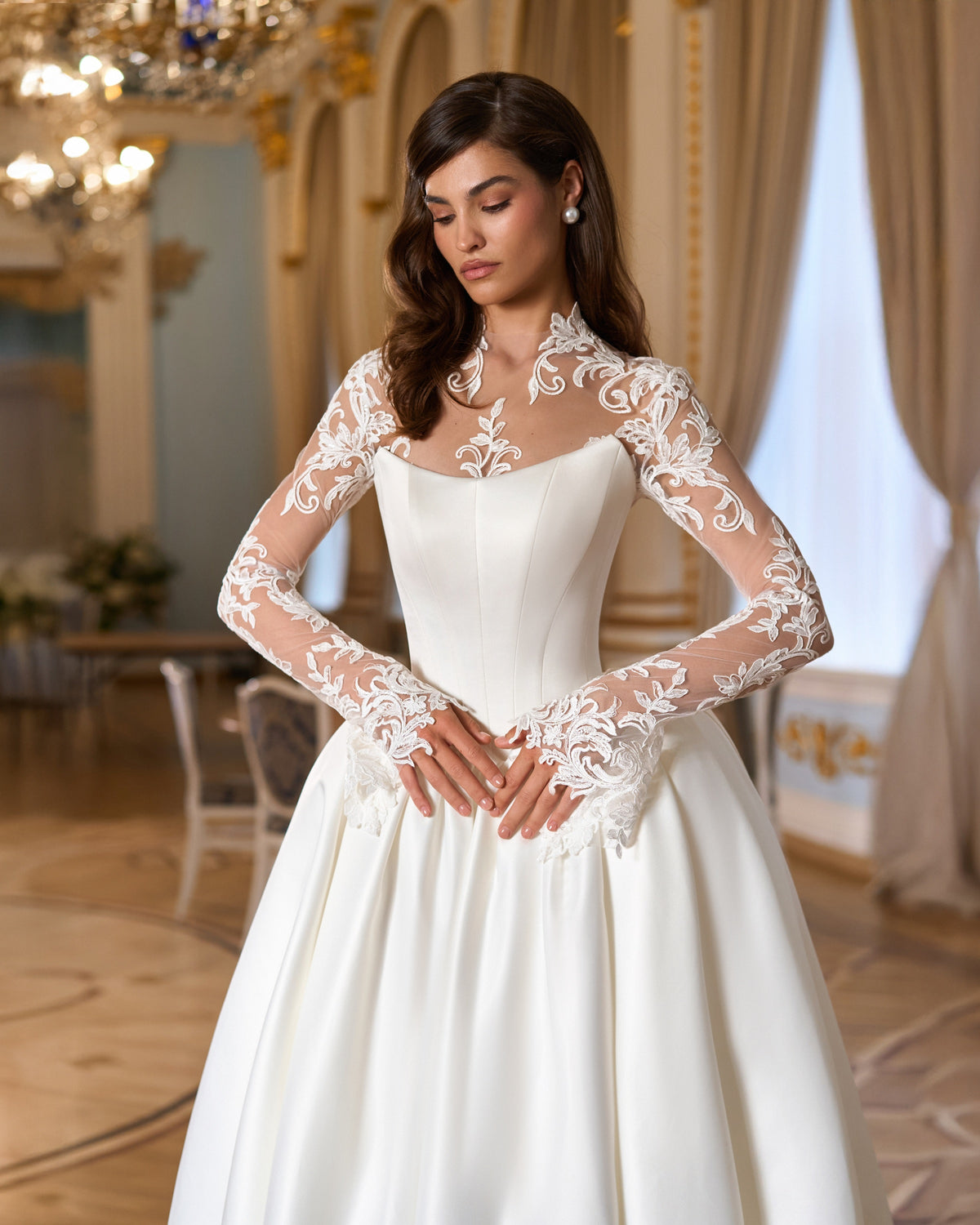 Front view of the structured curved-neckline bodice, pointed basque waist and floral lace layer with long sleeves.