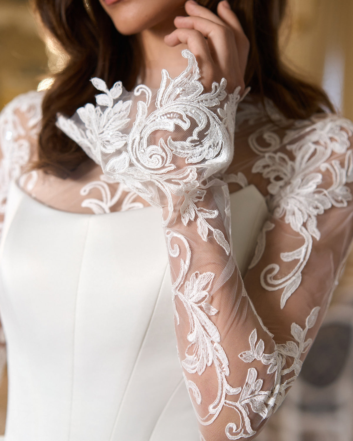 Close-up of the ornate floral lace cuff and sheer sleeve above the curved neckline of the wedding dress.