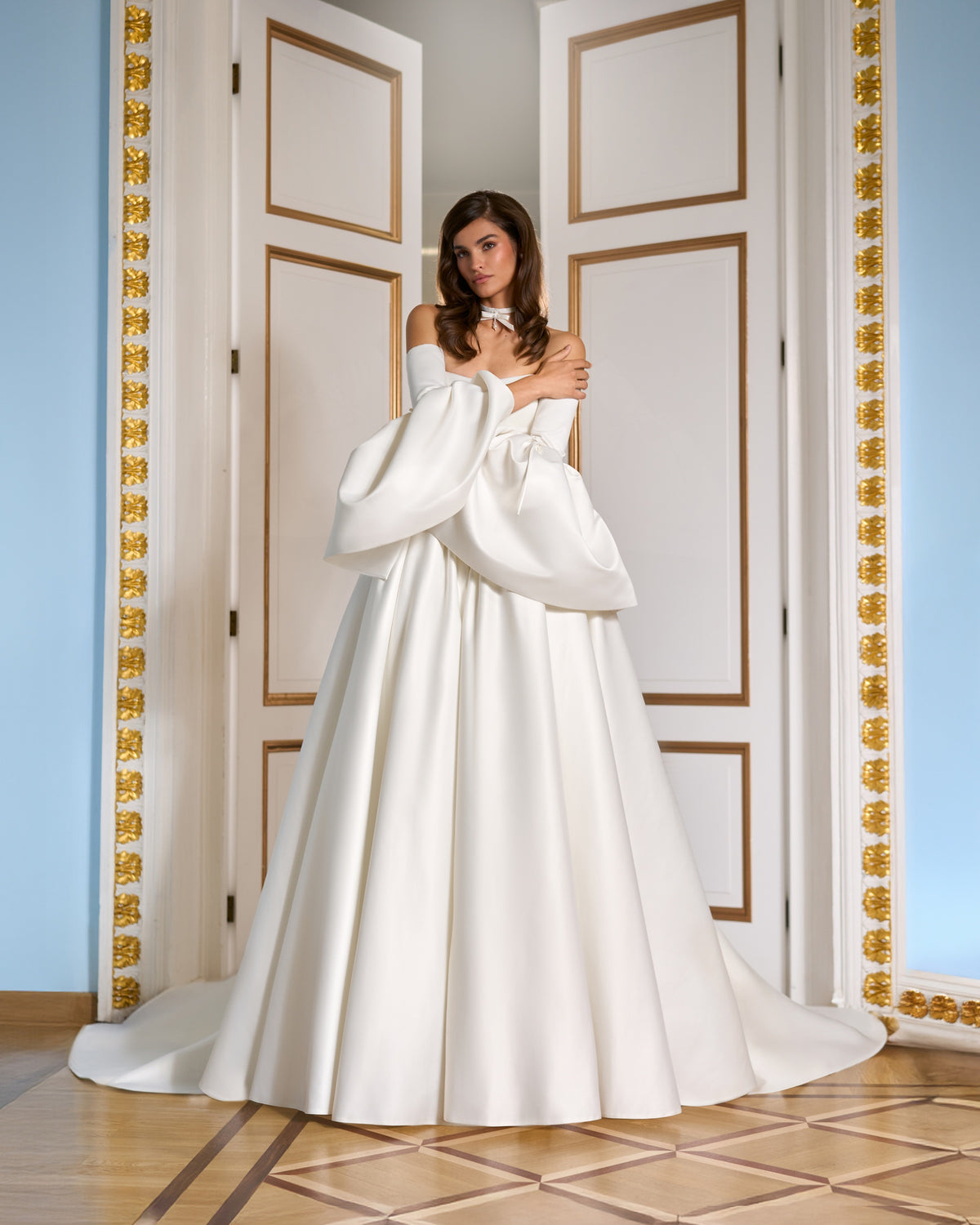 Ivory wedding dress shown full length with crossed arms, sculptural bell sleeves and a full skirt.