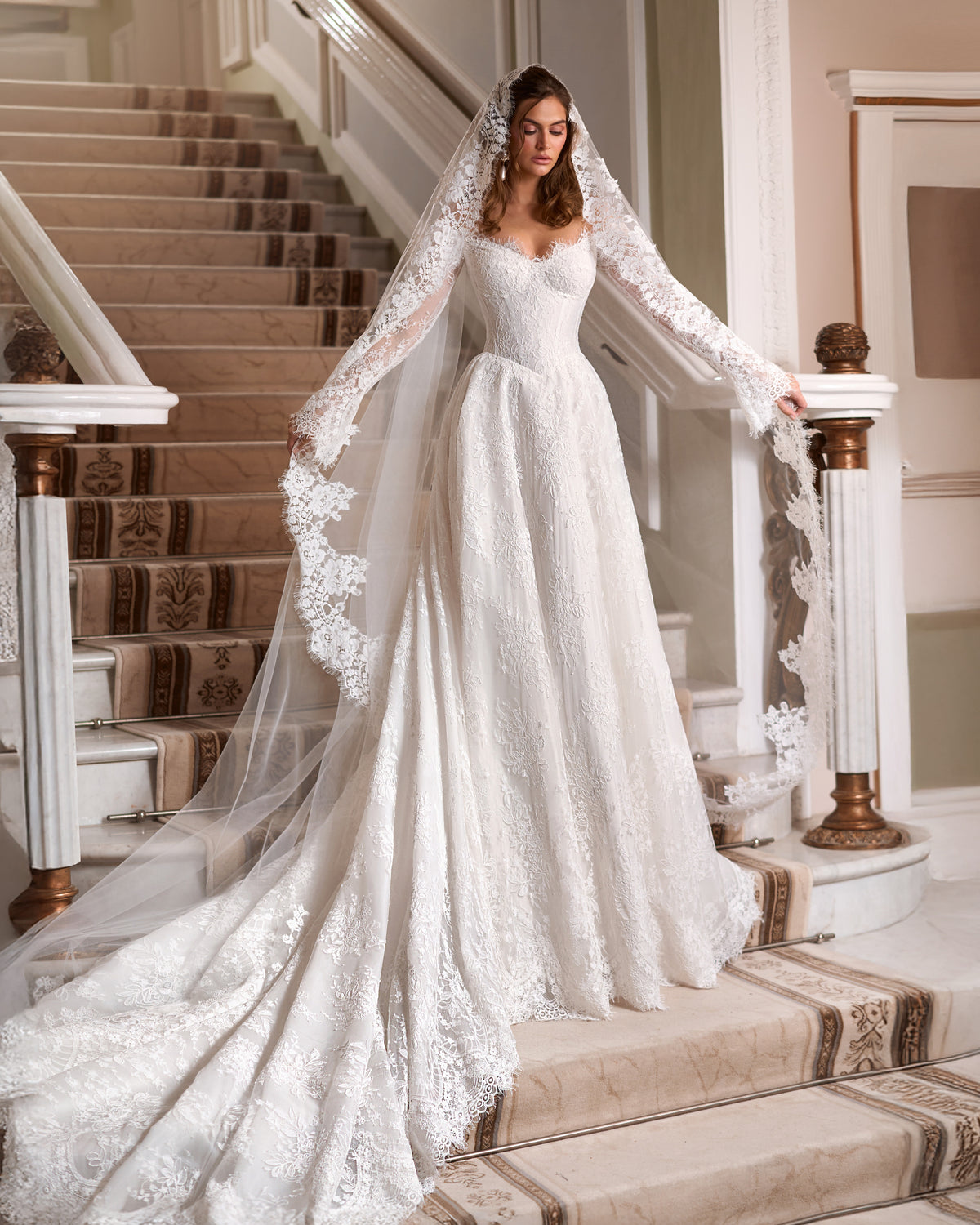 A-line lace wedding dress with an off-the-shoulder corset, long lace sleeves, a flowing train and a floral lace-edged veil.