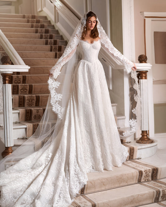 A-line lace wedding dress with an off-the-shoulder corset, long lace sleeves, a flowing train and a floral lace-edged veil.