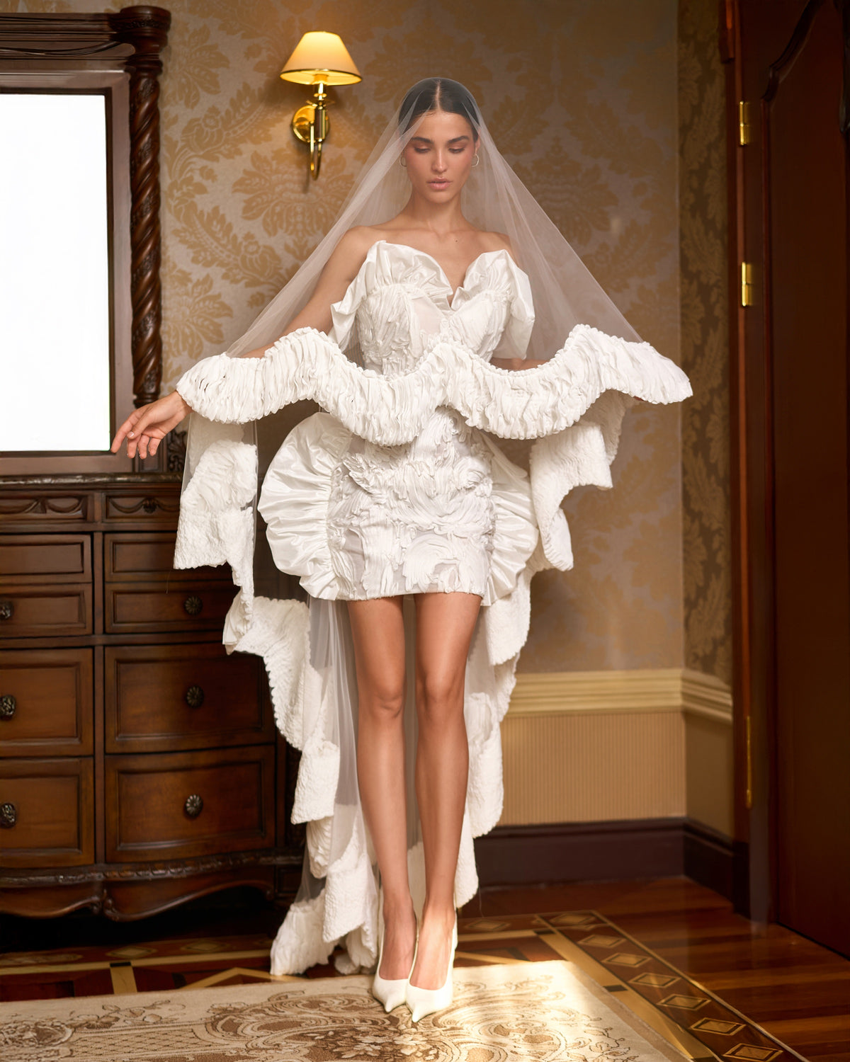 Mini wedding dress with a sweetheart neckline and sculptural ruffles beneath a long sheer, ruffle-edged cape-veil.
