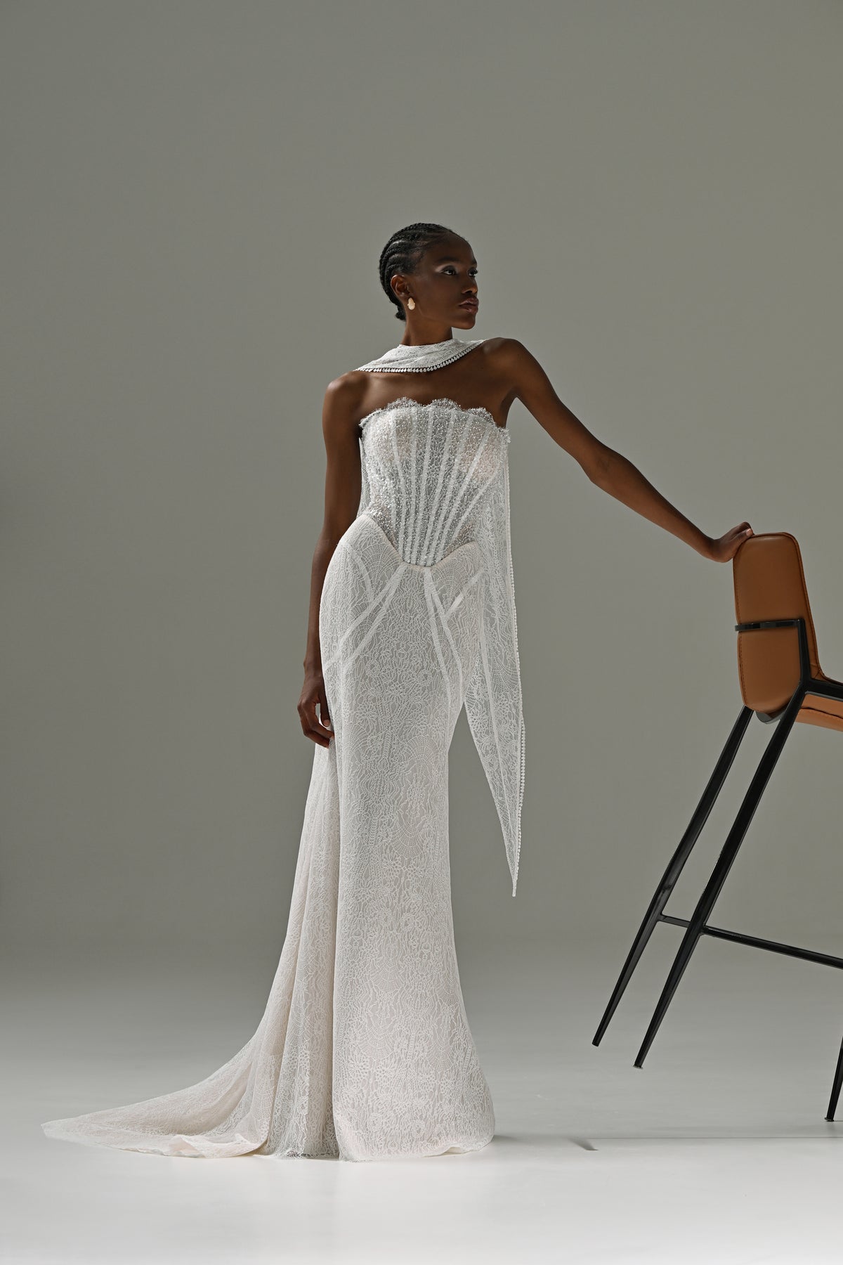 Strapless lace mermaid wedding dress with corset bodice and scarf collar – model leaning on a chair, full-length view