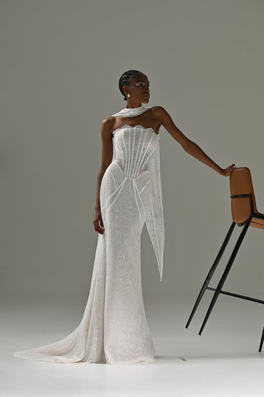 Strapless lace mermaid wedding dress with corset bodice and scarf collar – model leaning on a chair, full-length view