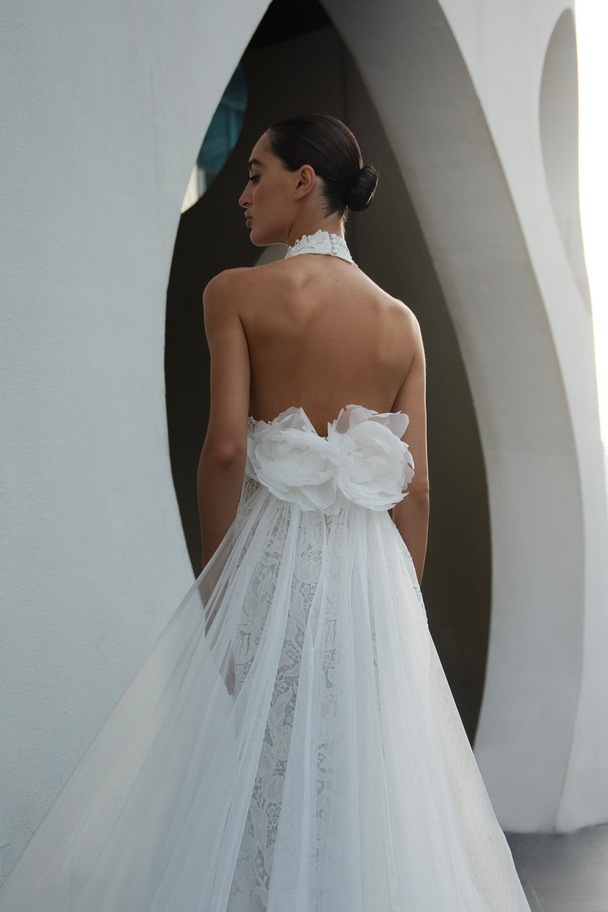 Backless halter lace sheath wedding dress with detachable tulle overskirt and cathedral train, photographed in the city.
