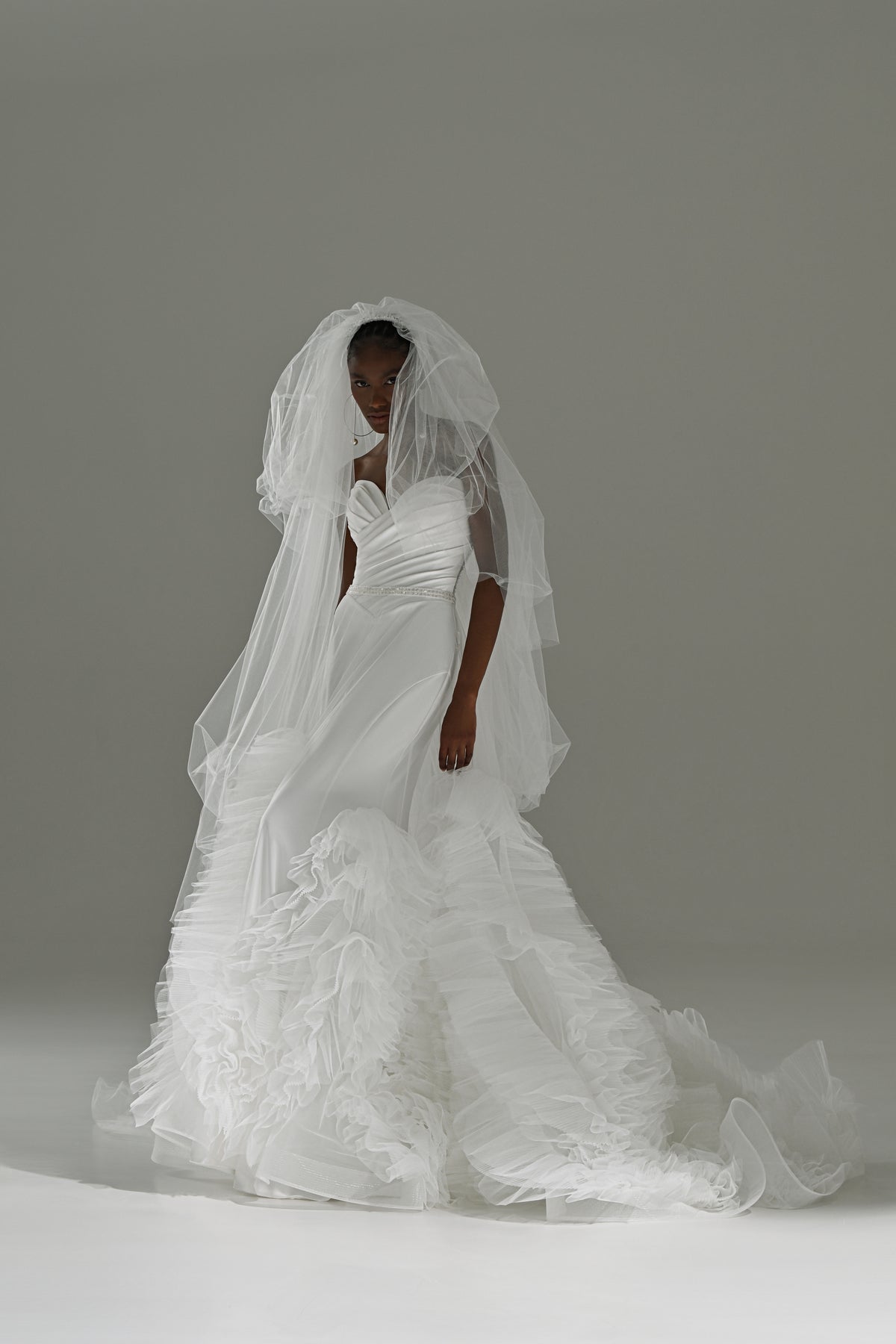 Stretch satin mermaid wedding dress with removable ruffled tulle skirt – front view with the veil over the face
