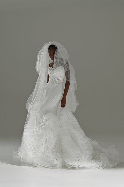 Stretch satin mermaid wedding dress with removable ruffled tulle skirt – front view with the veil over the face