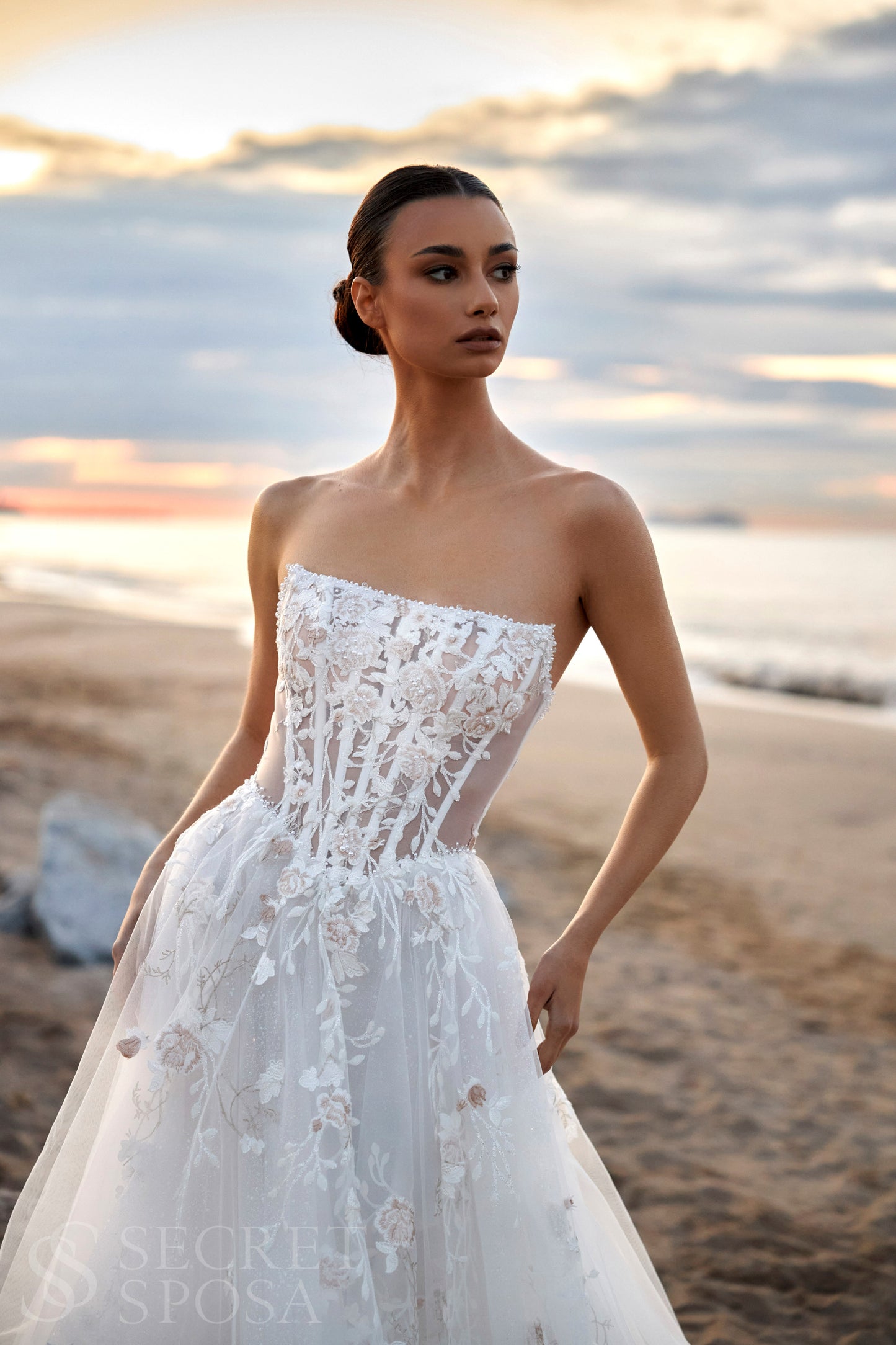 Bride in strapless floral lace and tulle A-line wedding gown with straight neckline, drop-down waist, and chapel train.