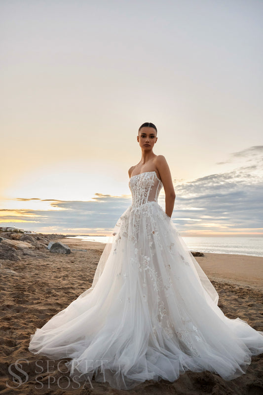 Bride in strapless floral lace and tulle A-line wedding gown with straight neckline, drop-down waist, and chapel train.