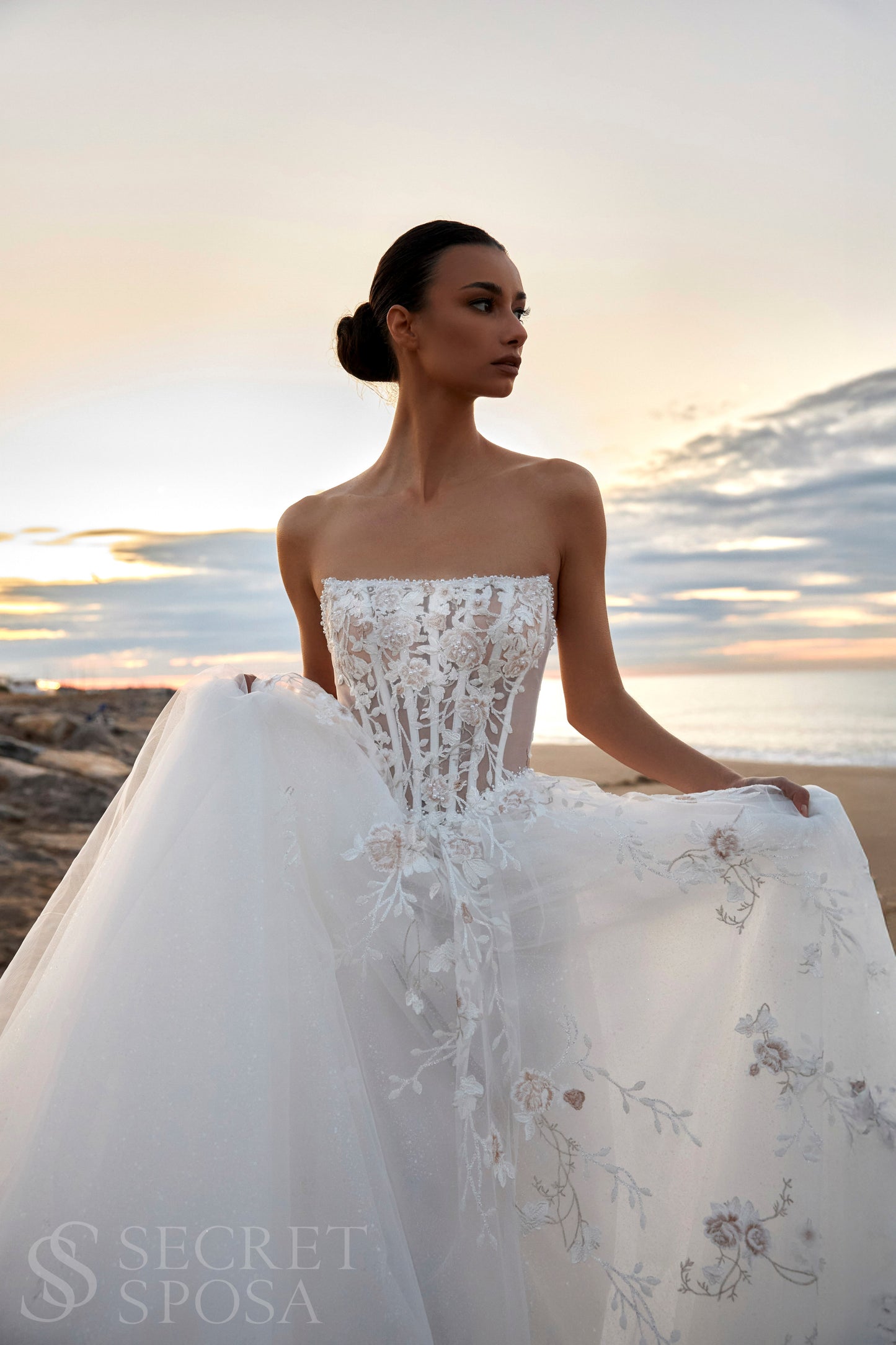 Bride in strapless floral lace and tulle A-line wedding gown with straight neckline, drop-down waist, and chapel train.