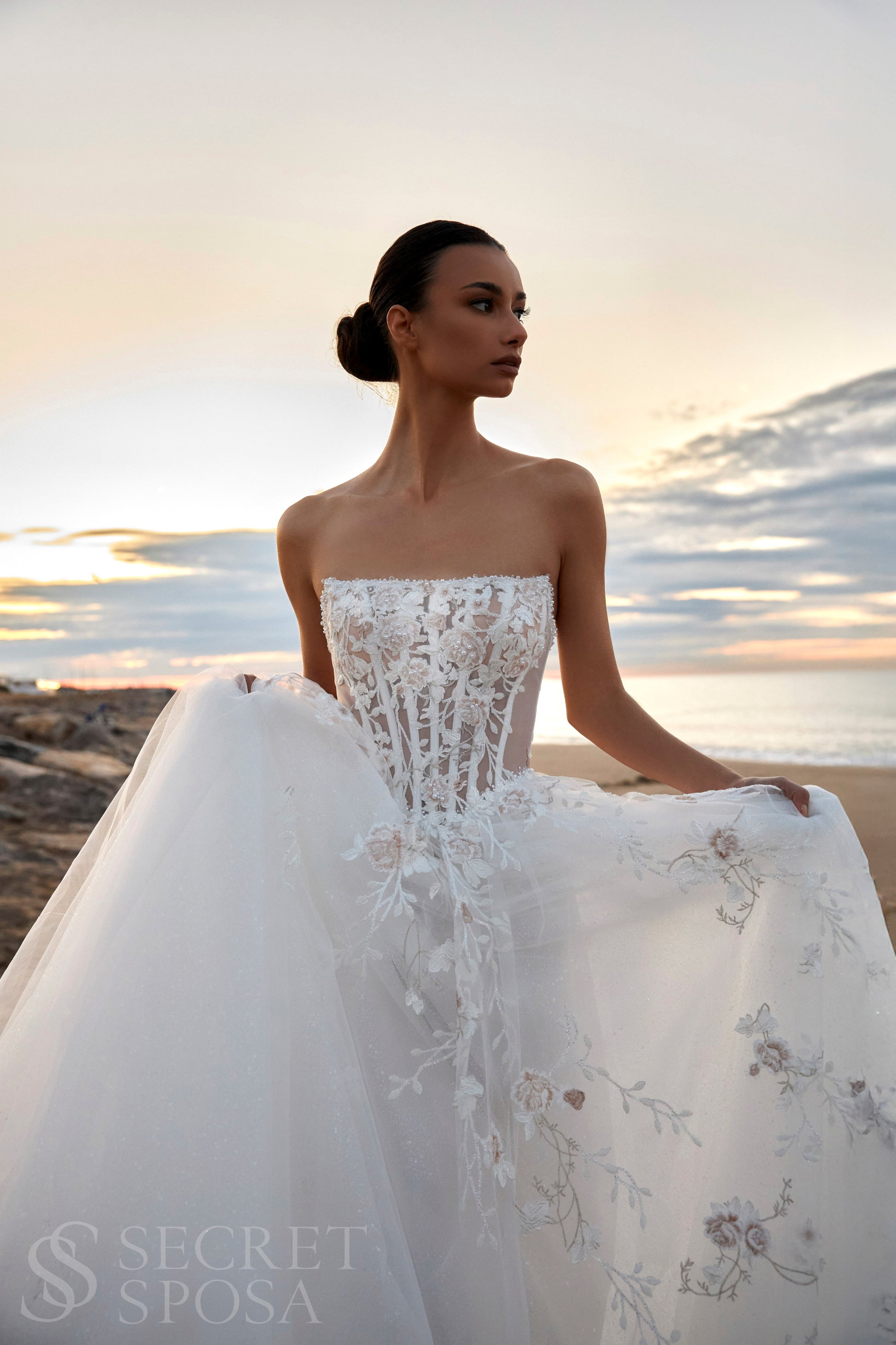 Bride in strapless floral lace and tulle A-line wedding gown with straight neckline, drop-down waist, and chapel train.