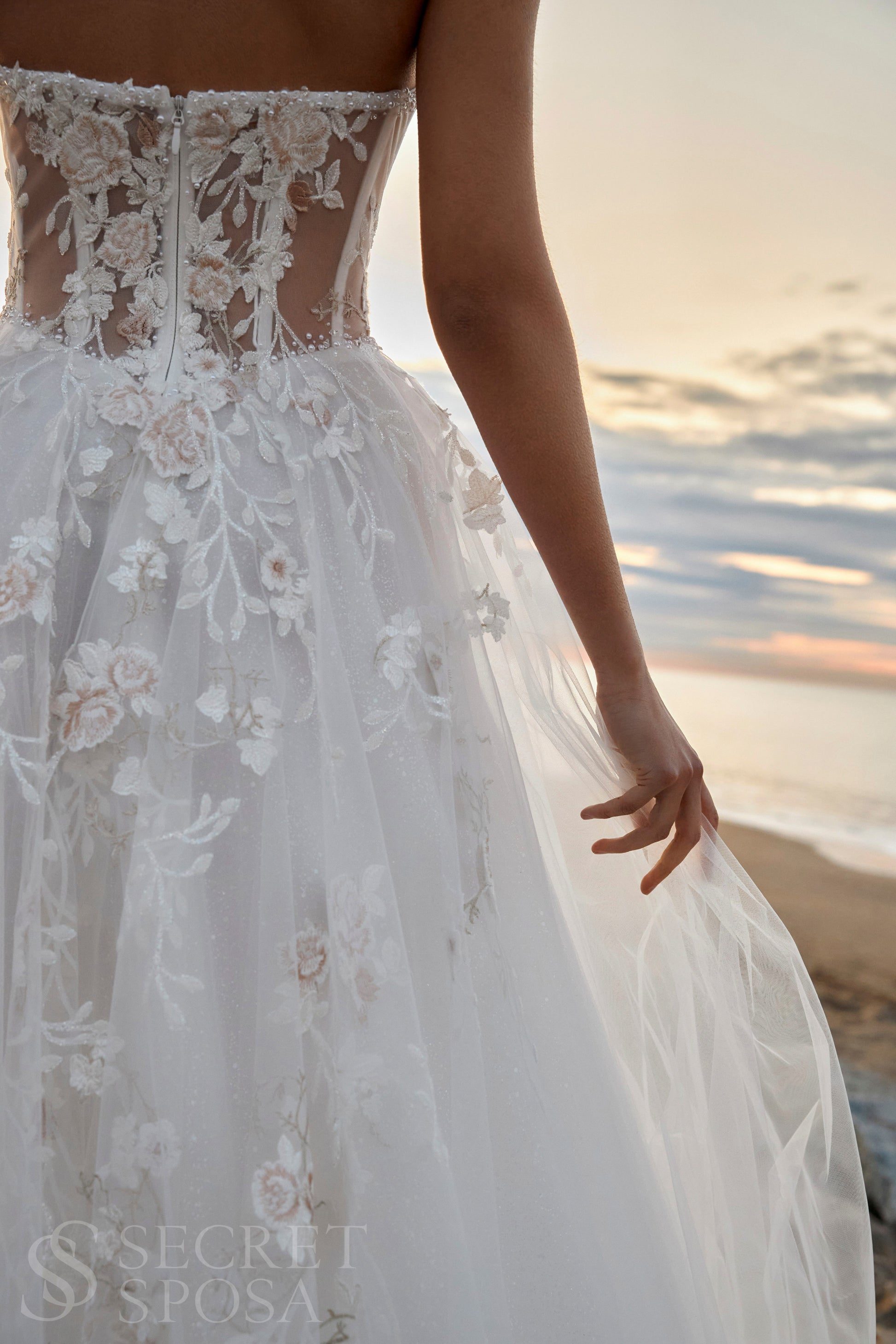 Bride in strapless floral lace and tulle A-line wedding gown with straight neckline, drop-down waist, and chapel train.
