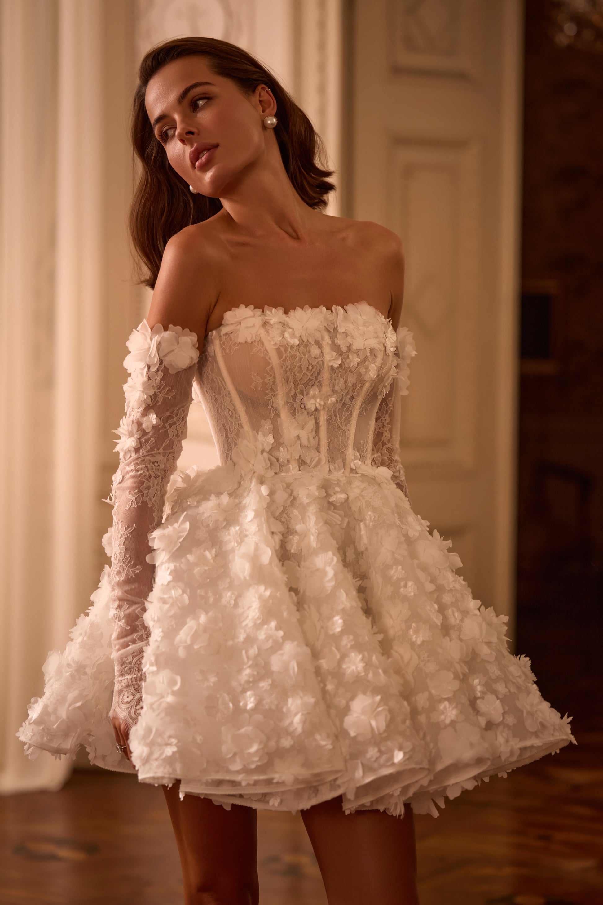 Bride in sleeveless mini A-line wedding dress with 3D floral lace, straight neckline, zip closure, and removable illusion sleeves, styled for reception or second look.