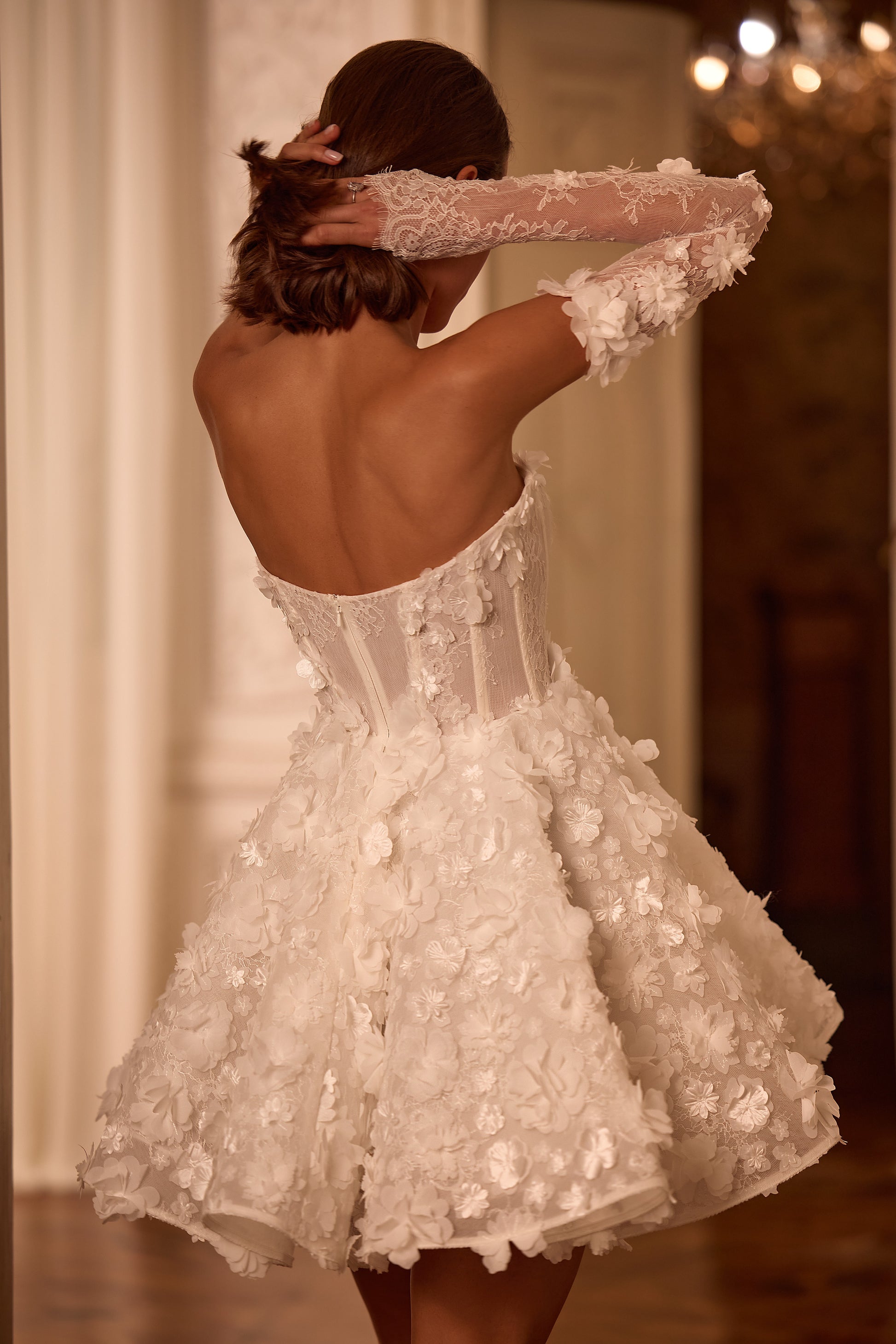 Bride in sleeveless mini A-line wedding dress with 3D floral lace, straight neckline, zip closure, and removable illusion sleeves, styled for reception or second look.
