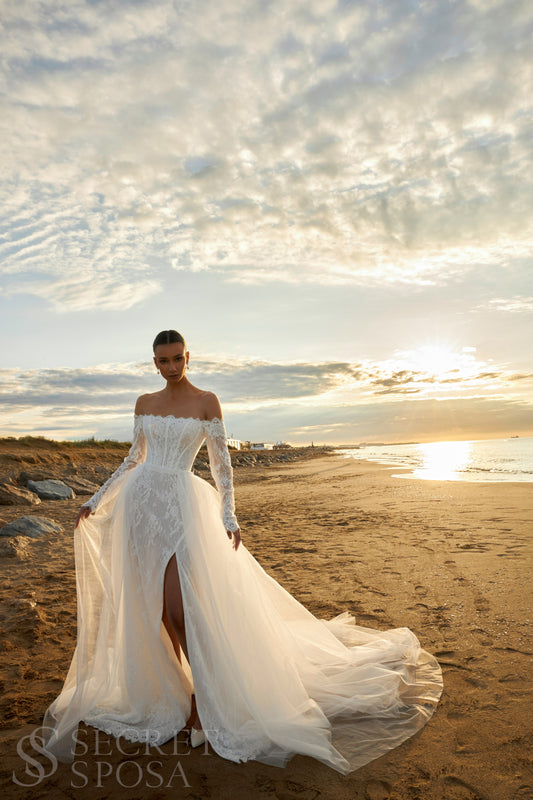 Bride in lace wedding dress with long off-the-shoulder sleeves, slit skirt, detachable tulle overskirt, open boat-shaped back, and sweep court train.