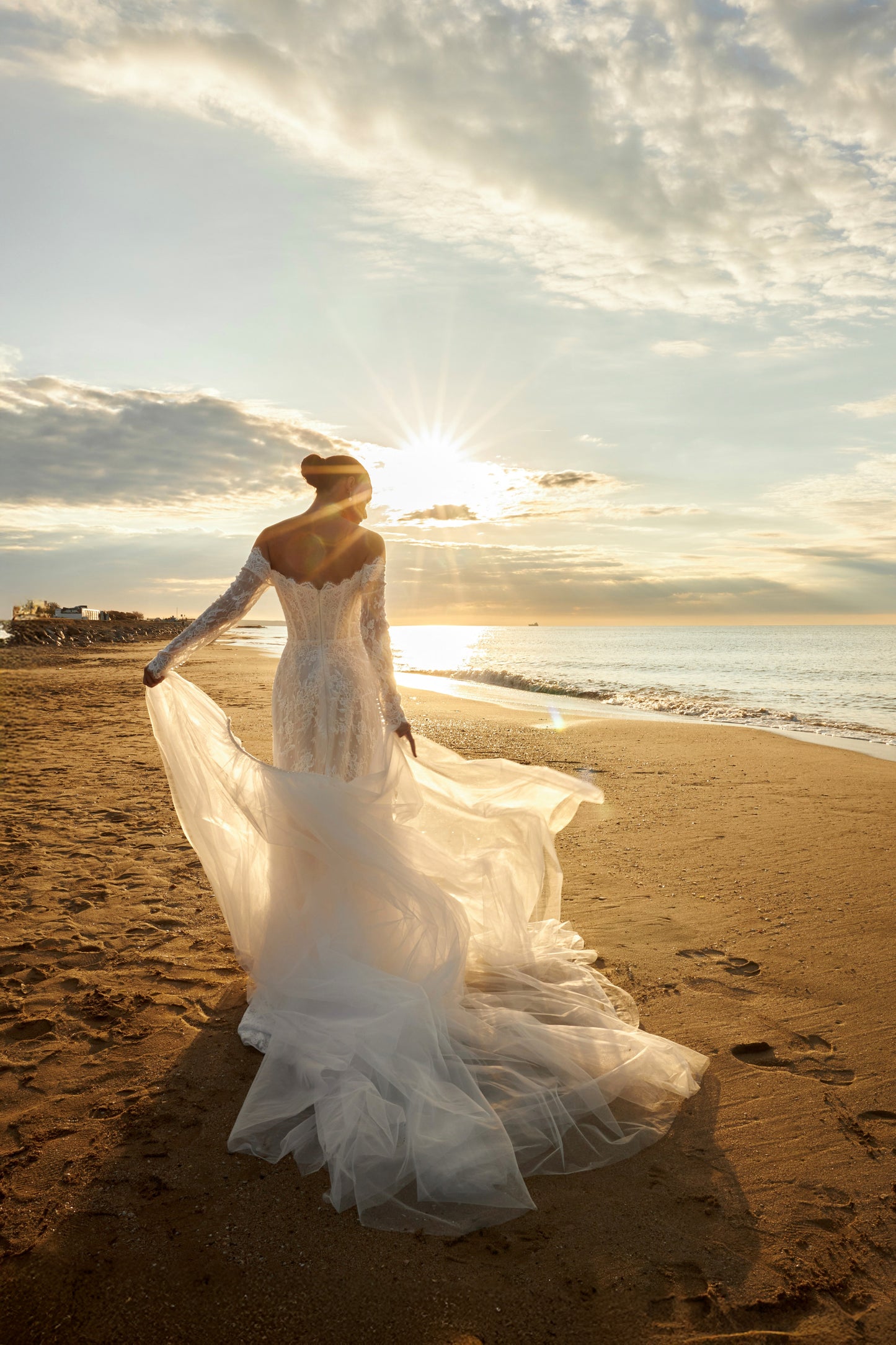 Bride in lace wedding dress with long off-the-shoulder sleeves, slit skirt, detachable tulle overskirt, open boat-shaped back, and sweep court train.