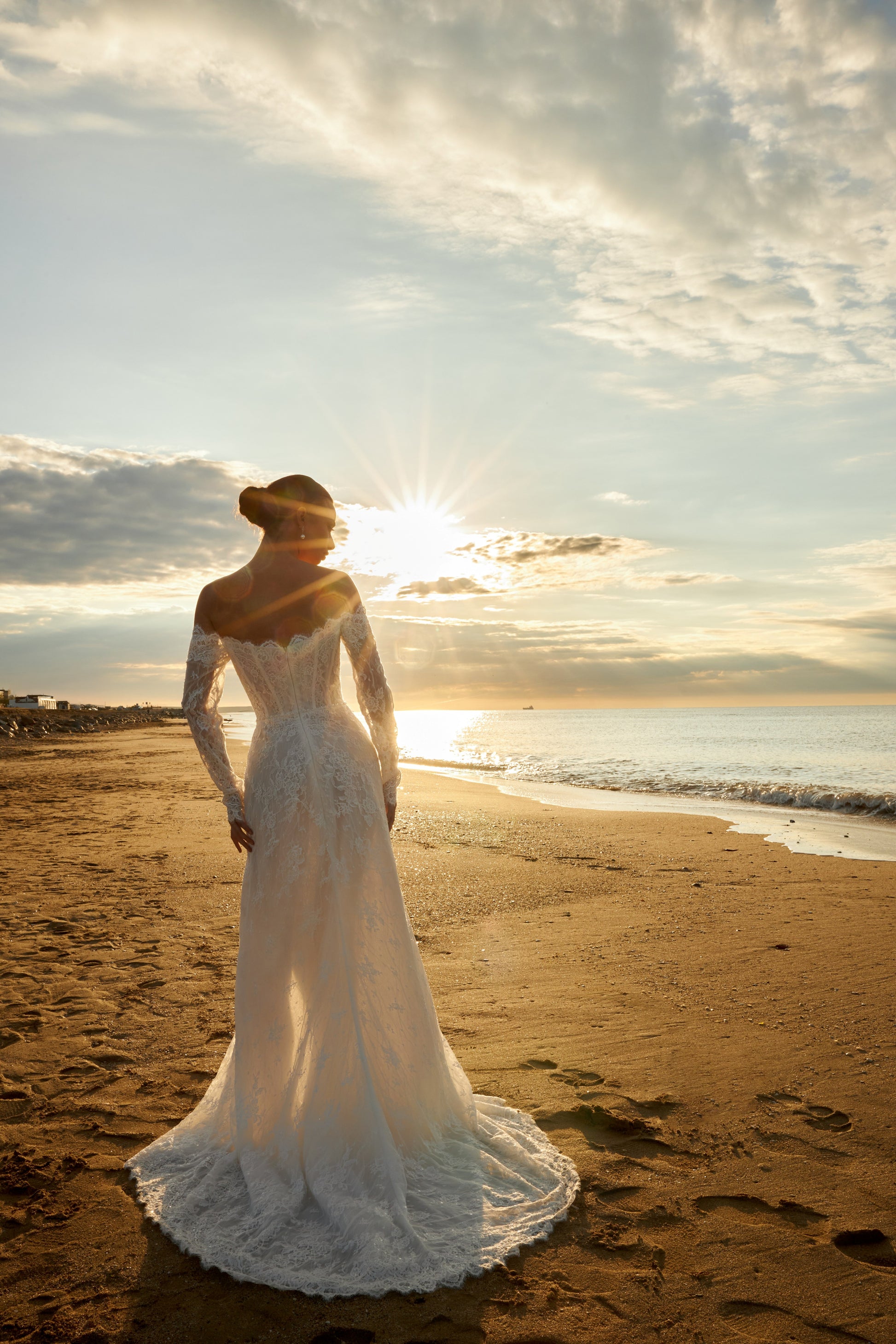 Bride in lace wedding dress with long off-the-shoulder sleeves, slit skirt, detachable tulle overskirt, open boat-shaped back, and sweep court train.