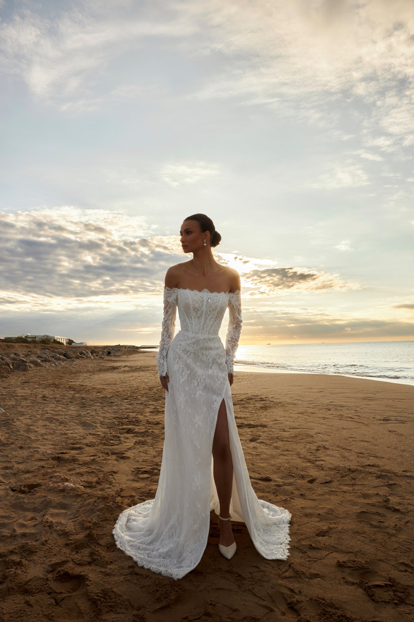 Bride in lace wedding dress with long off-the-shoulder sleeves, slit skirt, detachable tulle overskirt, open boat-shaped back, and sweep court train.