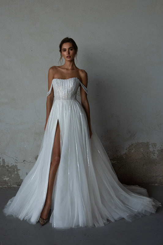 Pearl-embroidered tulle wedding dress with beaded corset bodice, detachable sheer sleeves, thigh-high slit, and flowing layered skirt
