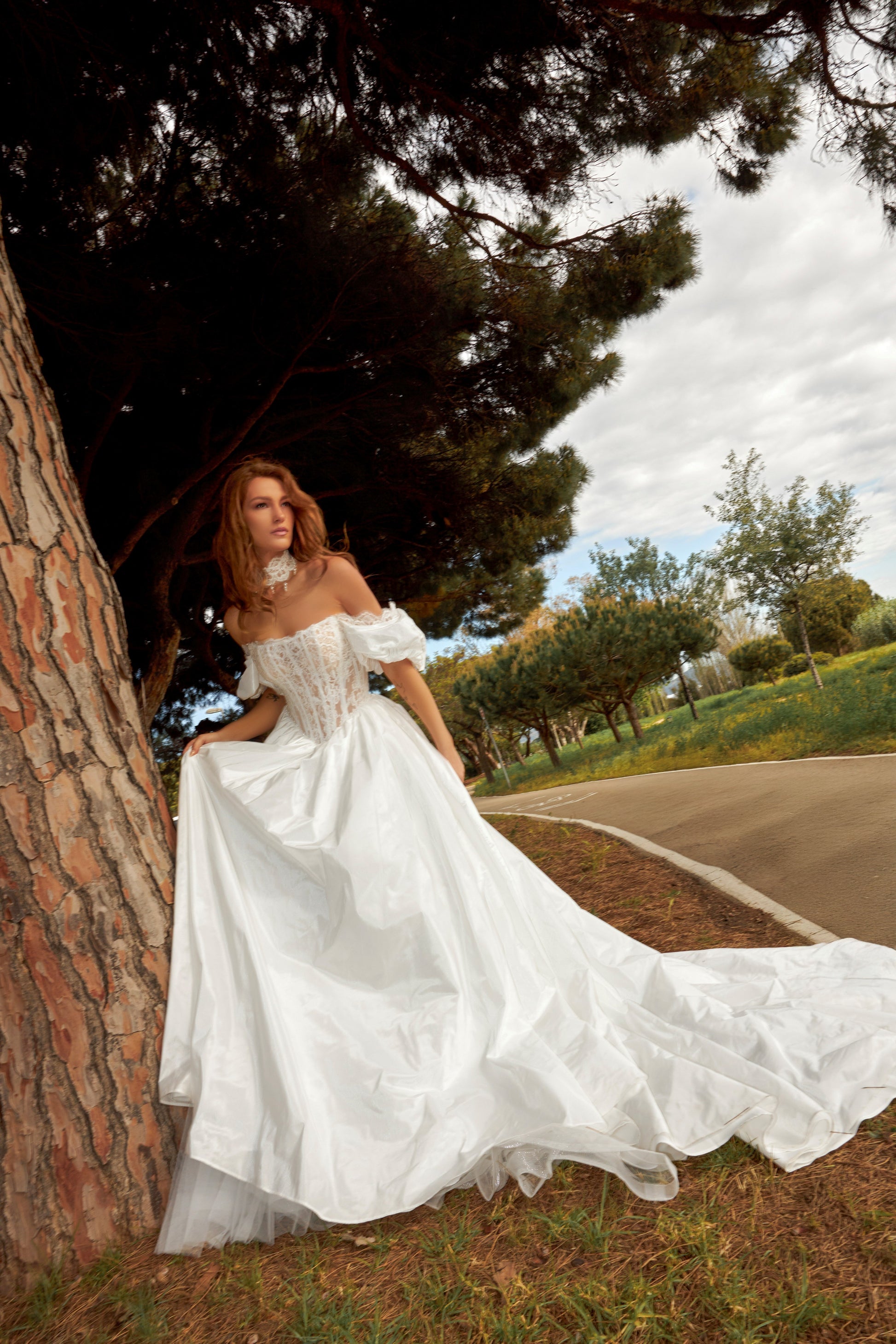 Bride in princess A-line wedding gown with puffy off-shoulder sleeves, lace bodice, lace-up waist, plain taffeta skirt, and cathedral train.