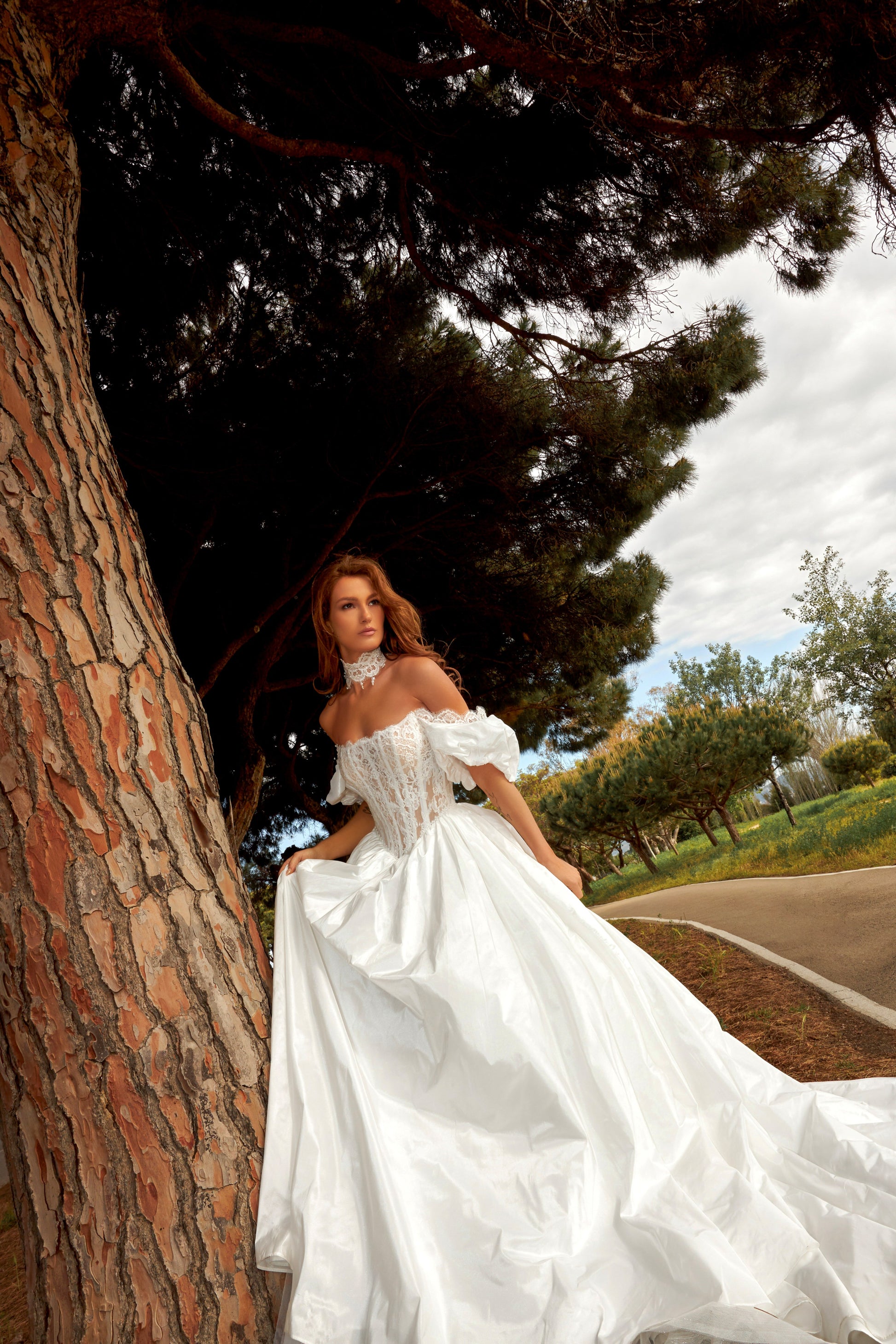 Bride in princess A-line wedding gown with puffy off-shoulder sleeves, lace bodice, lace-up waist, plain taffeta skirt, and cathedral train.