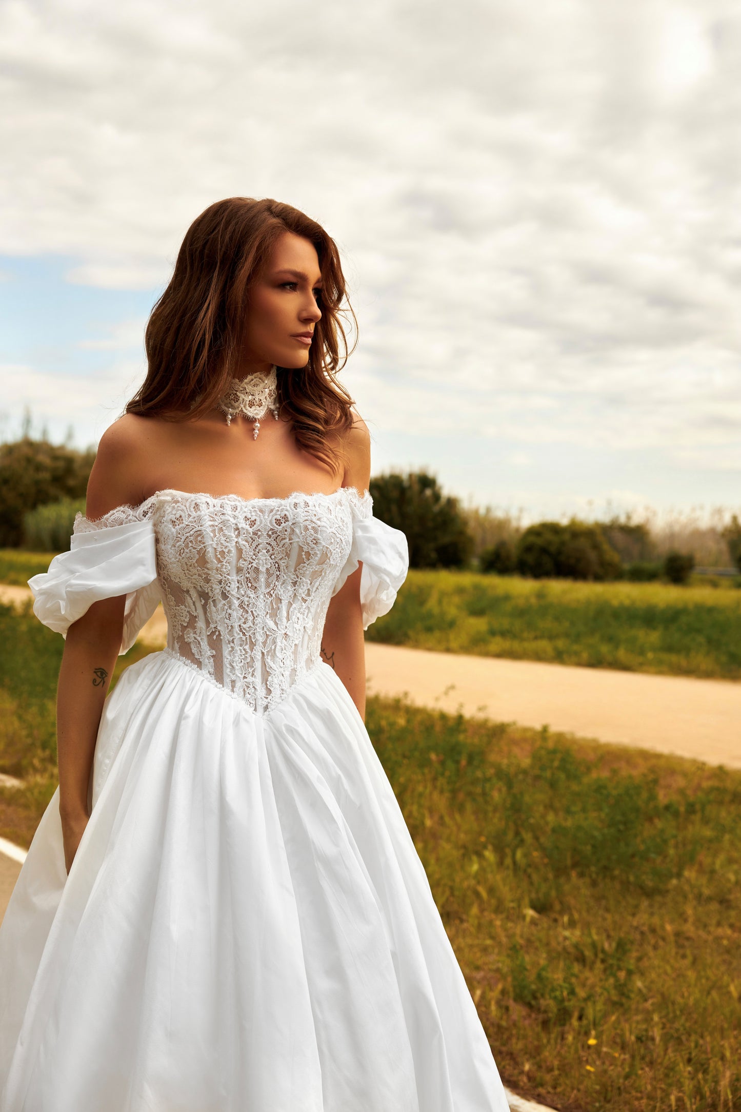 Bride in princess A-line wedding gown with puffy off-shoulder sleeves, lace bodice, lace-up waist, plain taffeta skirt, and cathedral train.