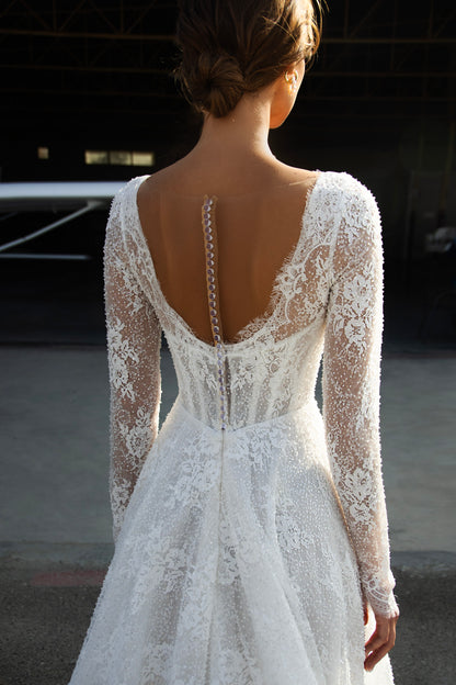 Sequin lace A-line wedding dress featuring long sheer sleeves, illusion scoop back with button-up closure, drop-down waist, and flowing court train