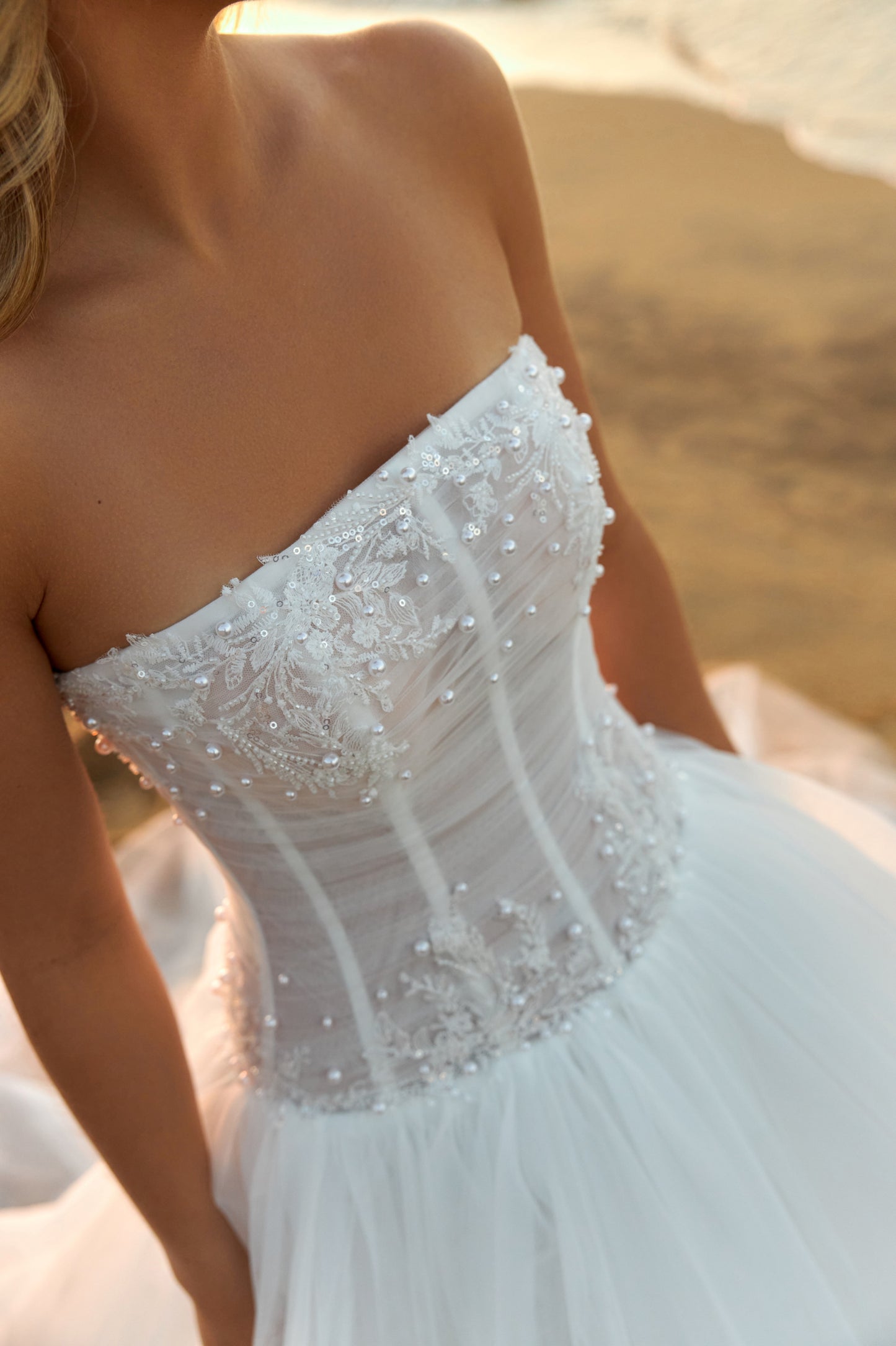 Bride in strapless soft tulle wedding gown with pearl and lace embellished prolonged bodice, zip closure, and chapel train.