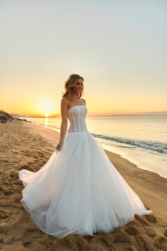 Bride in strapless soft tulle wedding gown with pearl and lace embellished prolonged bodice, zip closure, and chapel train.