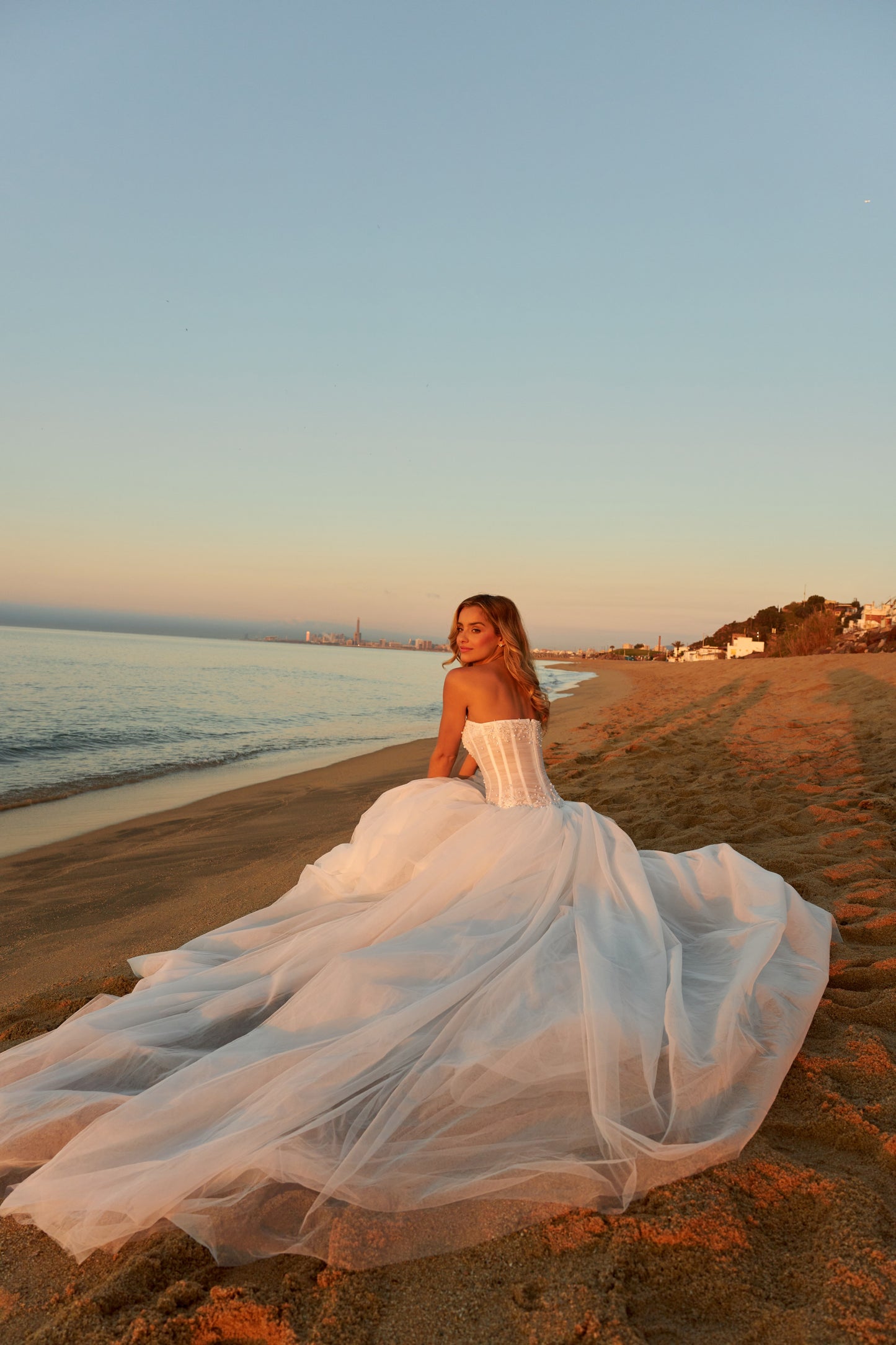Bride in strapless soft tulle wedding gown with pearl and lace embellished prolonged bodice, zip closure, and chapel train.