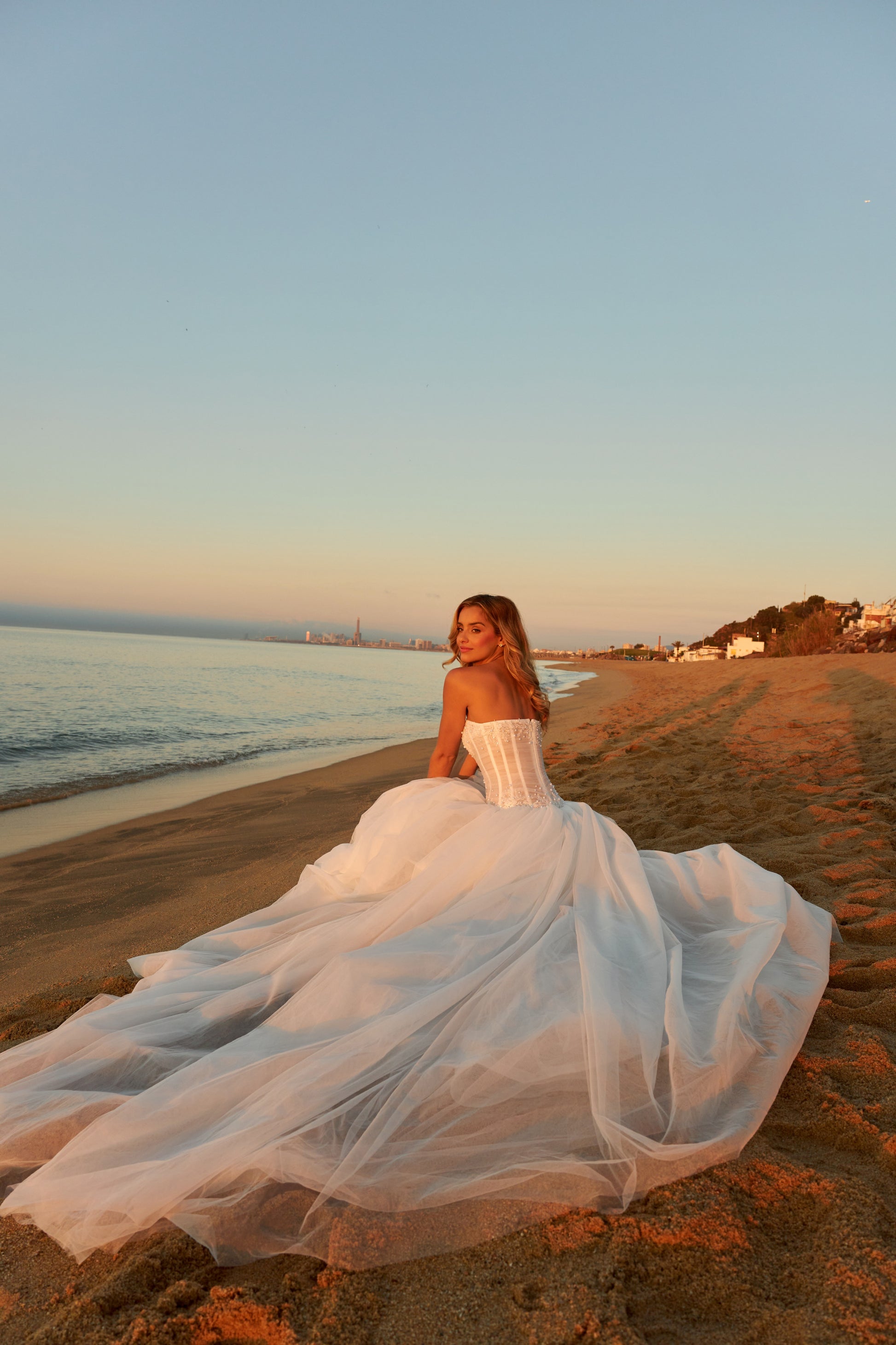 Bride in strapless soft tulle wedding gown with pearl and lace embellished prolonged bodice, zip closure, and chapel train.