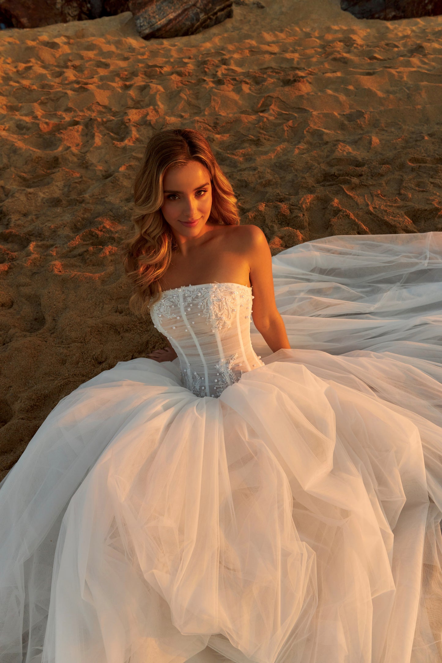 Bride in strapless soft tulle wedding gown with pearl and lace embellished prolonged bodice, zip closure, and chapel train.