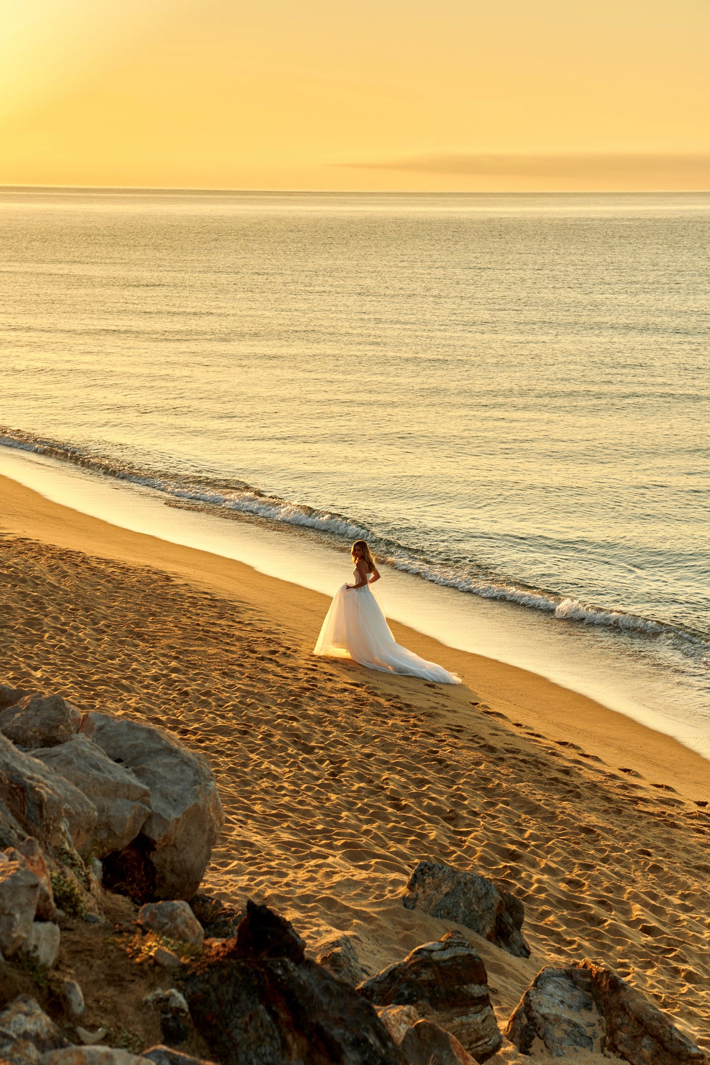 Bride in strapless soft tulle wedding gown with pearl and lace embellished prolonged bodice, zip closure, and chapel train.