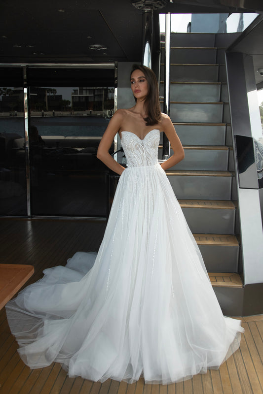 Bride wearing a beaded A-line wedding gown with sweetheart neckline and detachable illusion bolero featuring long sleeves and open back.