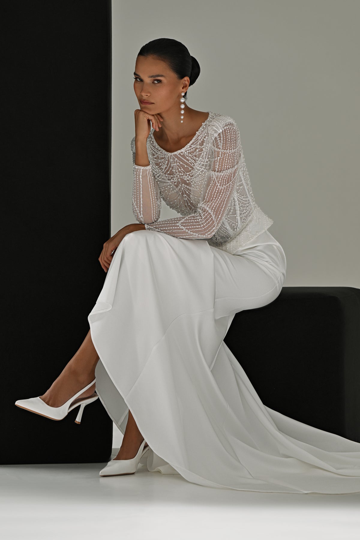 Beaded lace sheath wedding dress with long sleeves – model seated on a black block, train spread on the floor