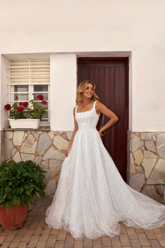 Bride wearing an A-line tulle wedding dress with square neckline, pearl and sequin embroidered lace bodice, glitter tulle skirt, and zip closure.
