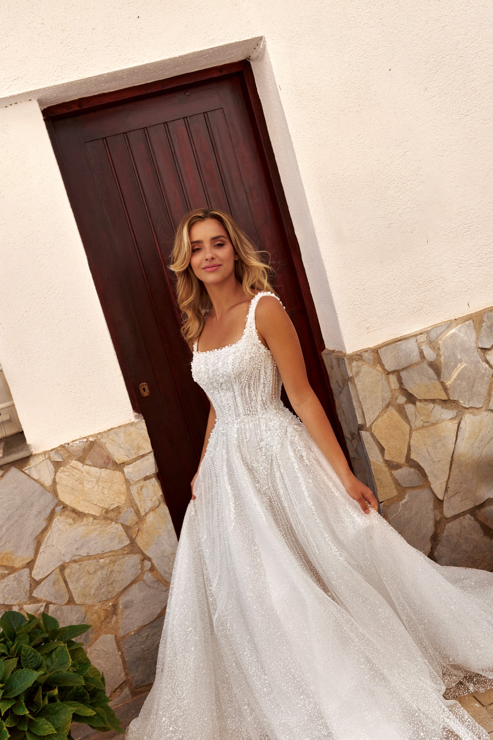 Bride wearing an A-line tulle wedding dress with square neckline, pearl and sequin embroidered lace bodice, glitter tulle skirt, and zip closure.