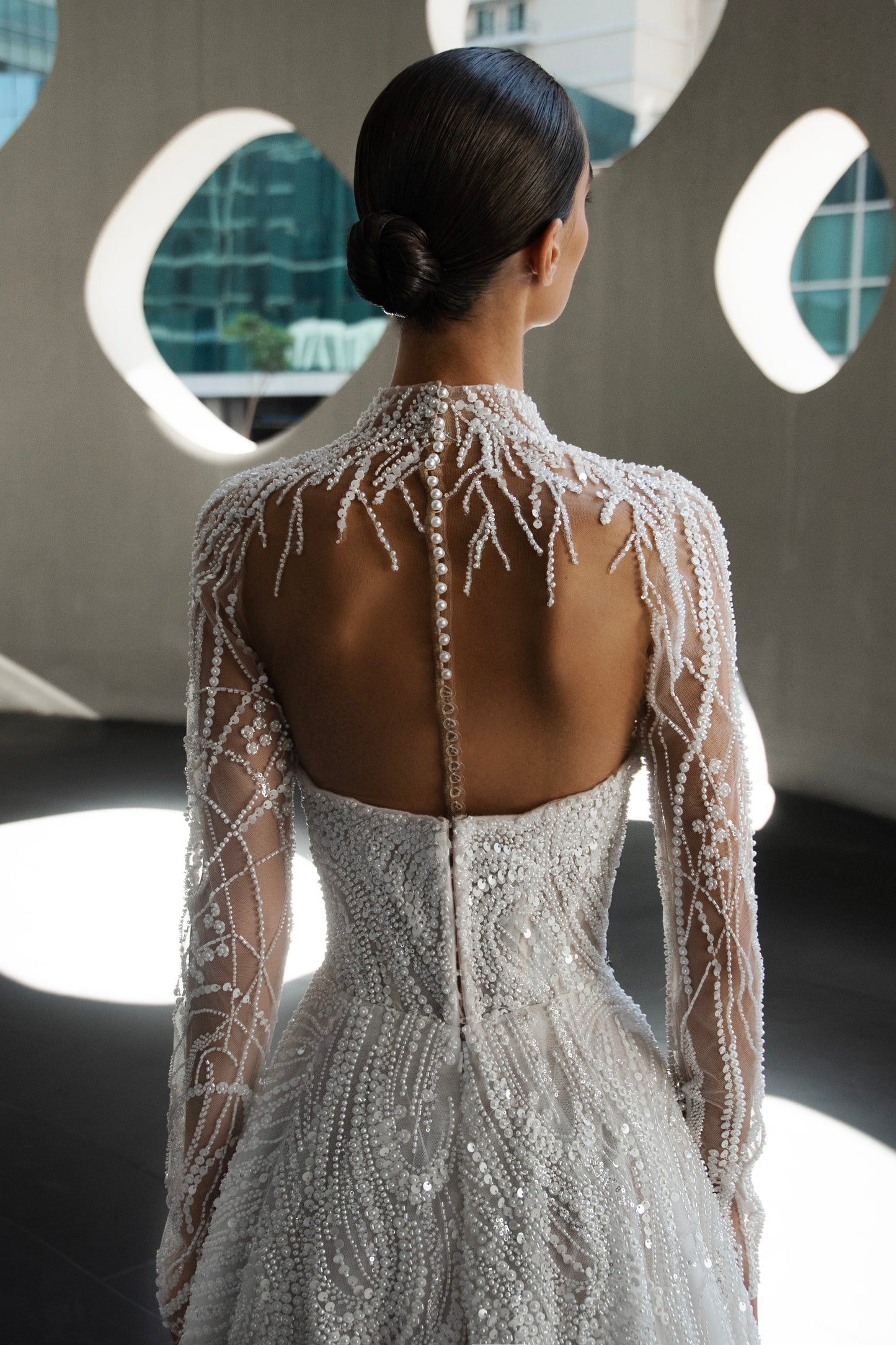 Back view of beaded A-line bridal gown with detachable illusion high-neck bolero, sheer long sleeves, button-back, and chapel train.