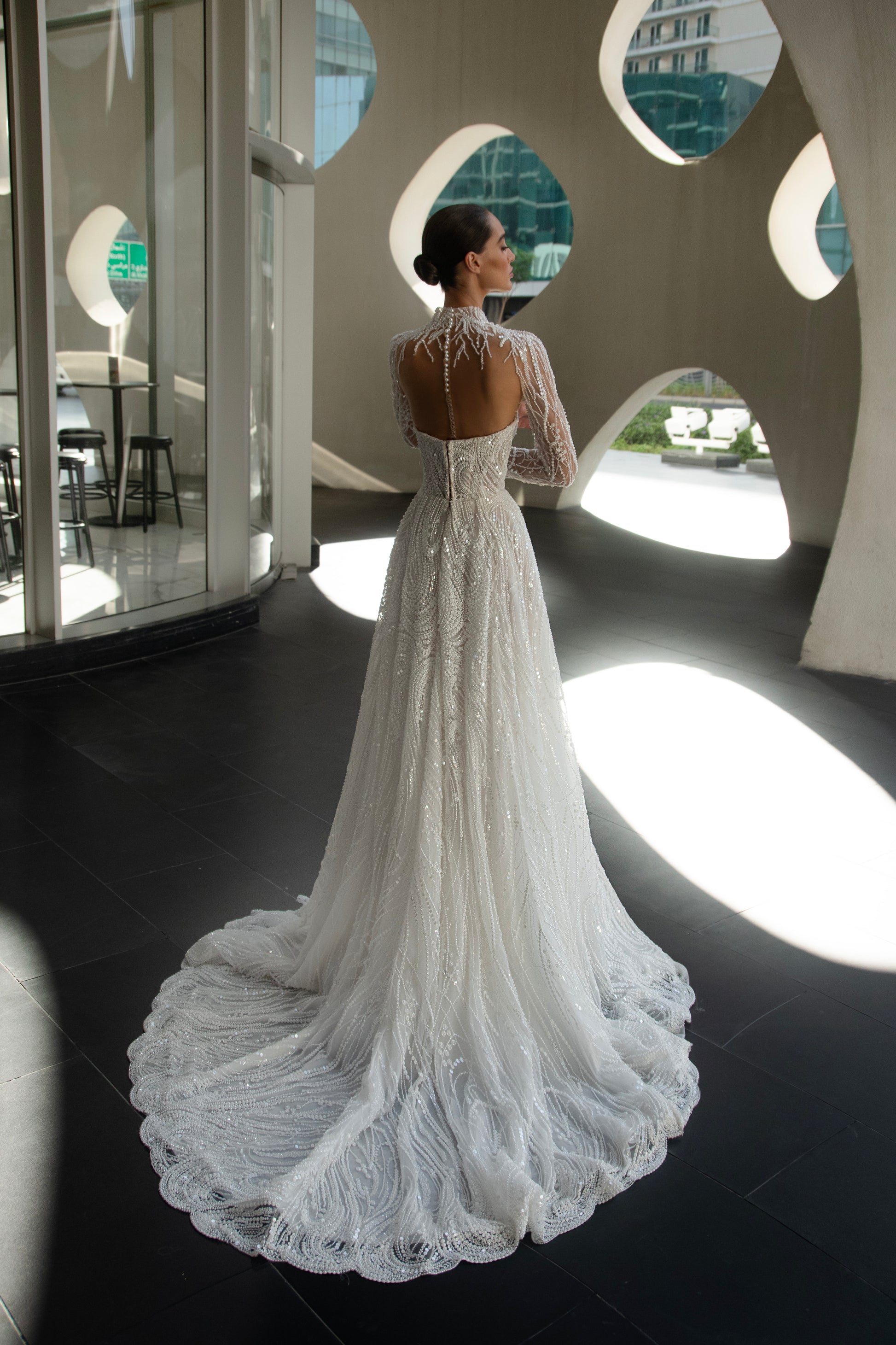 Back view of beaded A-line bridal gown with detachable illusion high-neck bolero, sheer long sleeves, button-back, and chapel train.