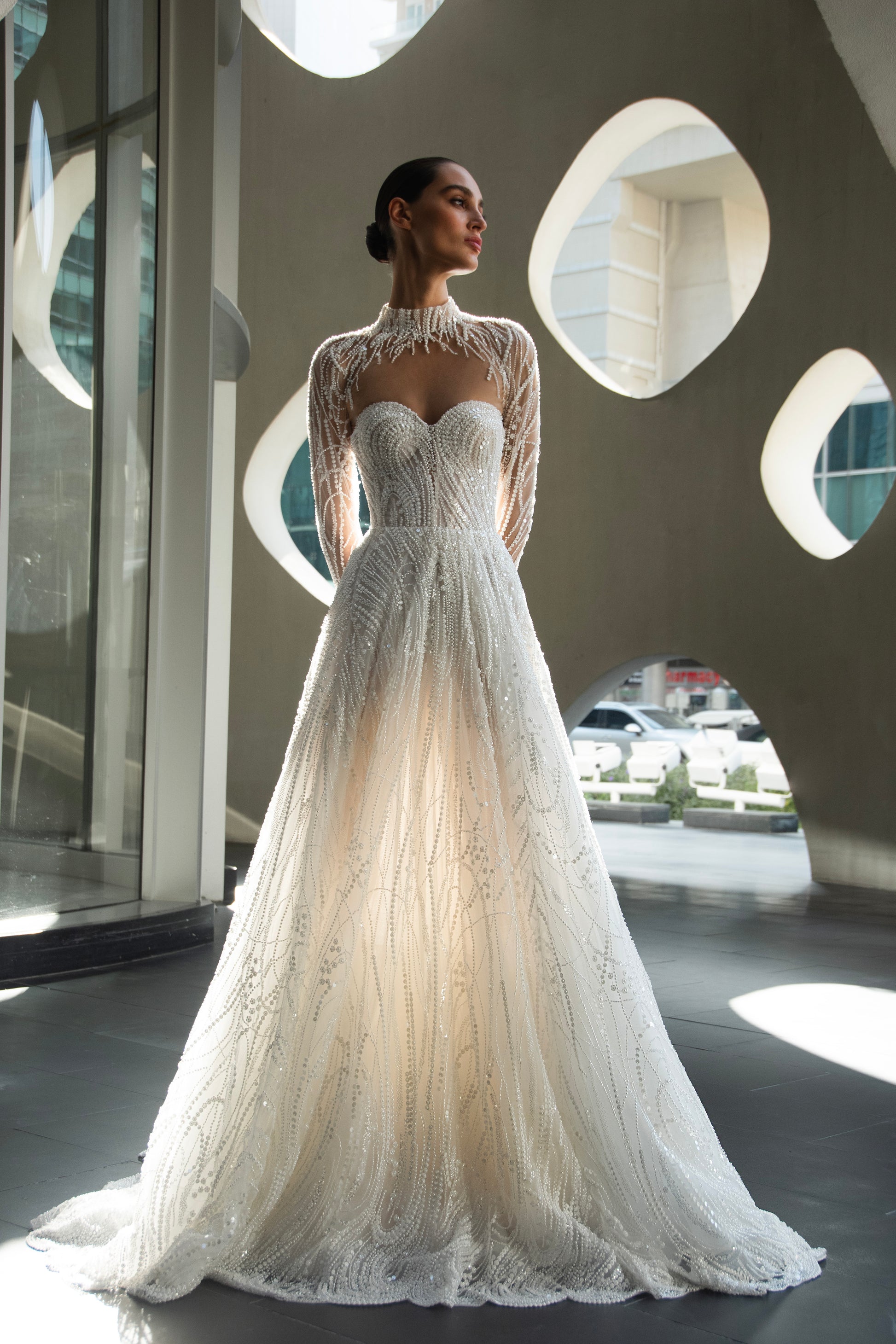 Back view of beaded A-line bridal gown with detachable illusion high-neck bolero, sheer long sleeves, button-back, and chapel train.