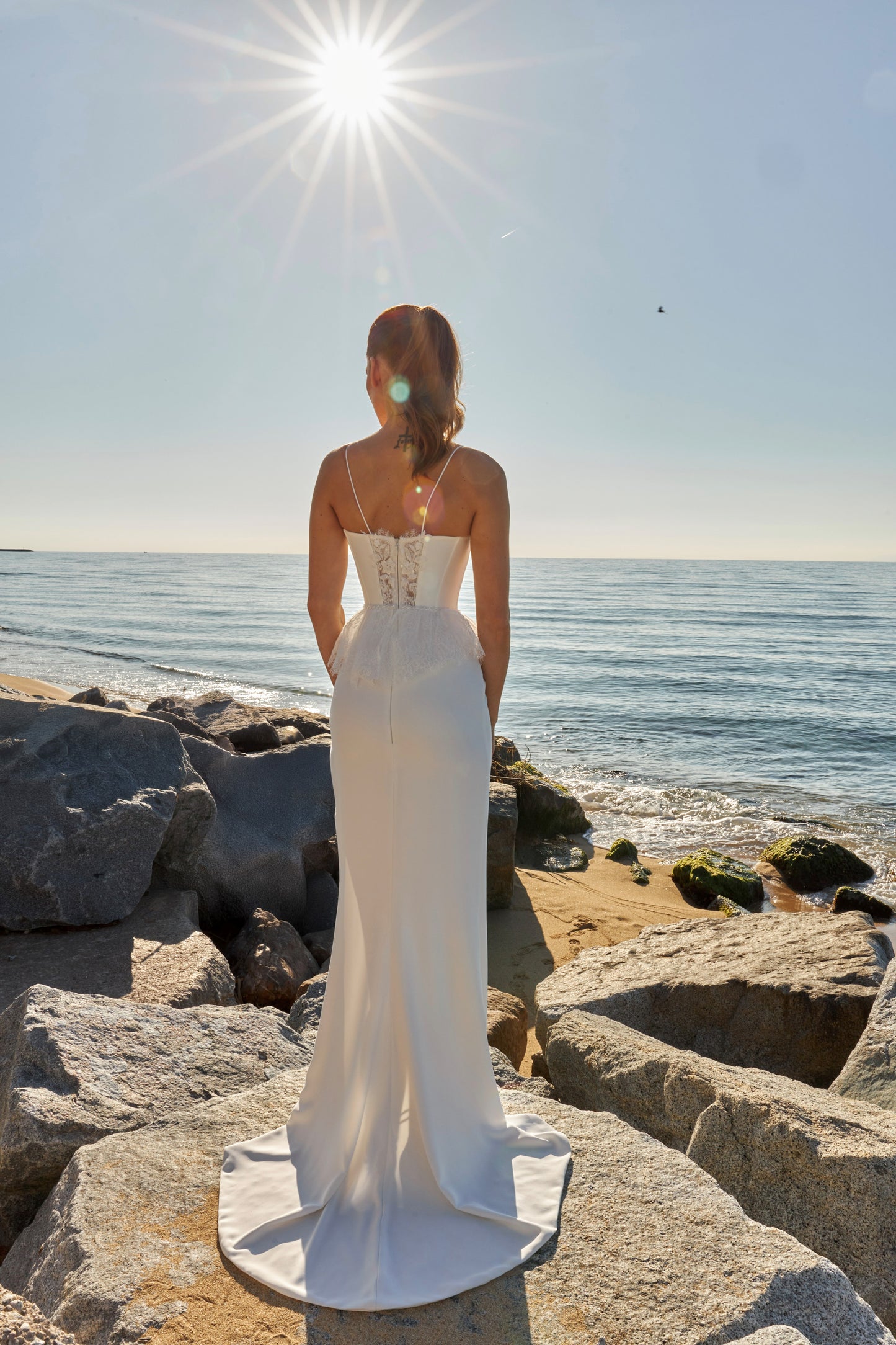 Bride in sleeveless sheath wedding gown with lace bodice, spaghetti straps, slit skirt, zip closure, and sweep train.