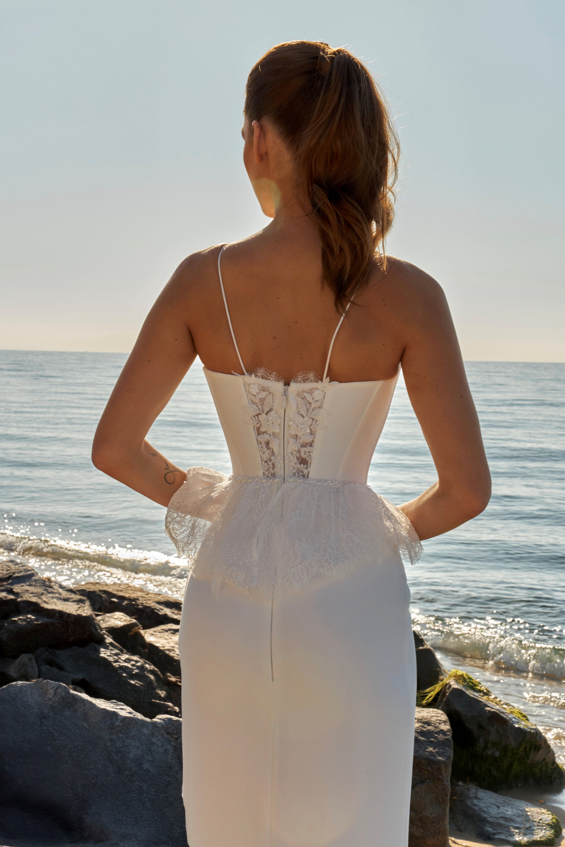 Bride in sleeveless sheath wedding gown with lace bodice, spaghetti straps, slit skirt, zip closure, and sweep train.