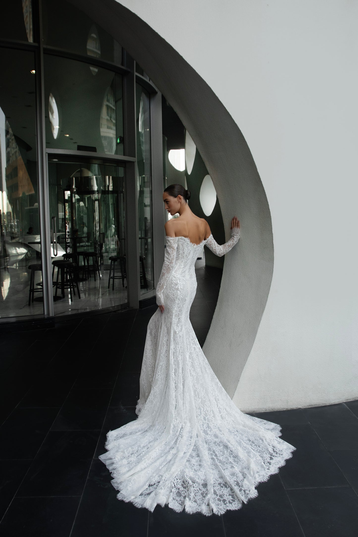 Off-shoulder lace wedding gown with long illusion sleeves, corset bodice, and chapel-length train.