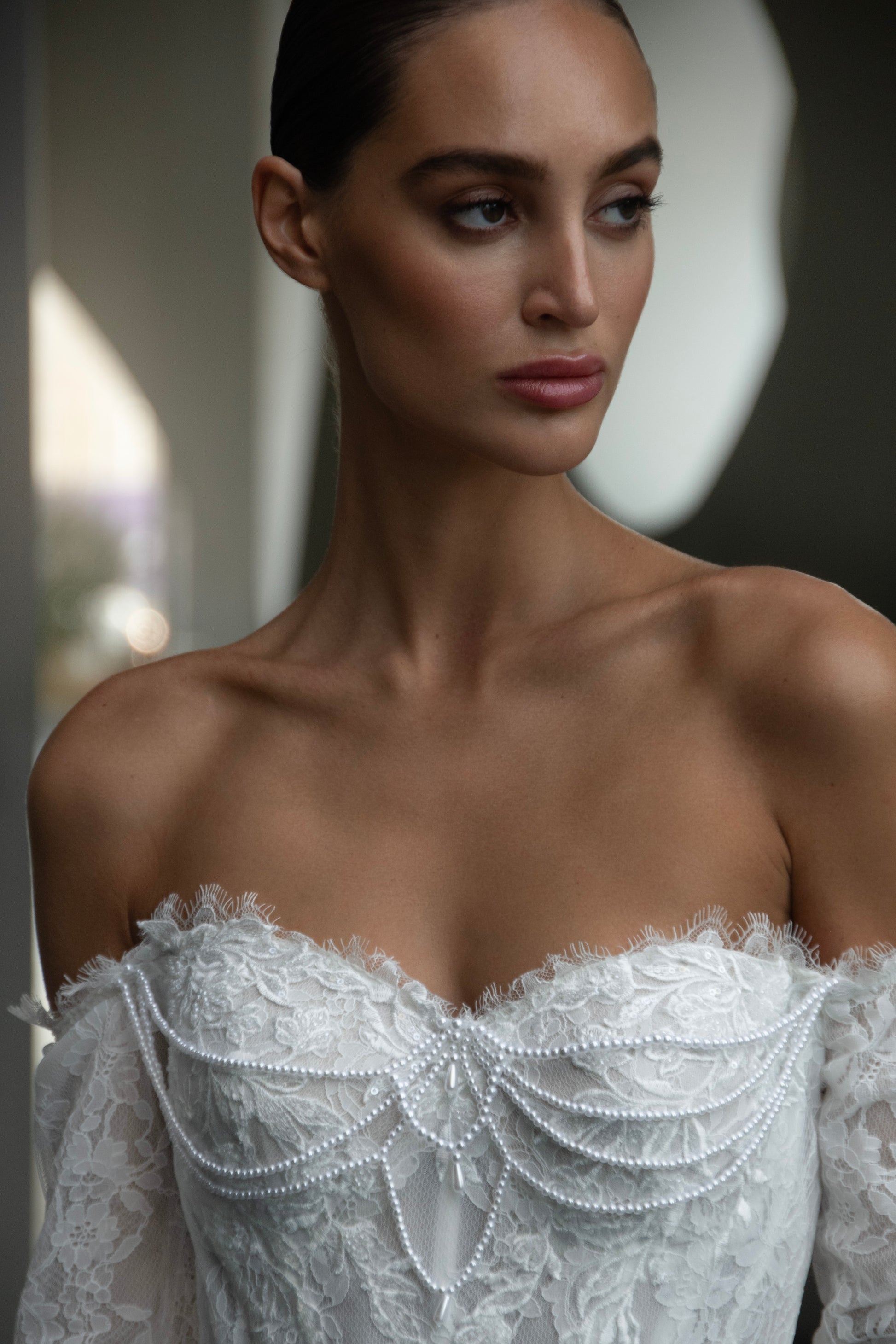 Off-shoulder lace wedding gown with long illusion sleeves, corset bodice, and chapel-length train.