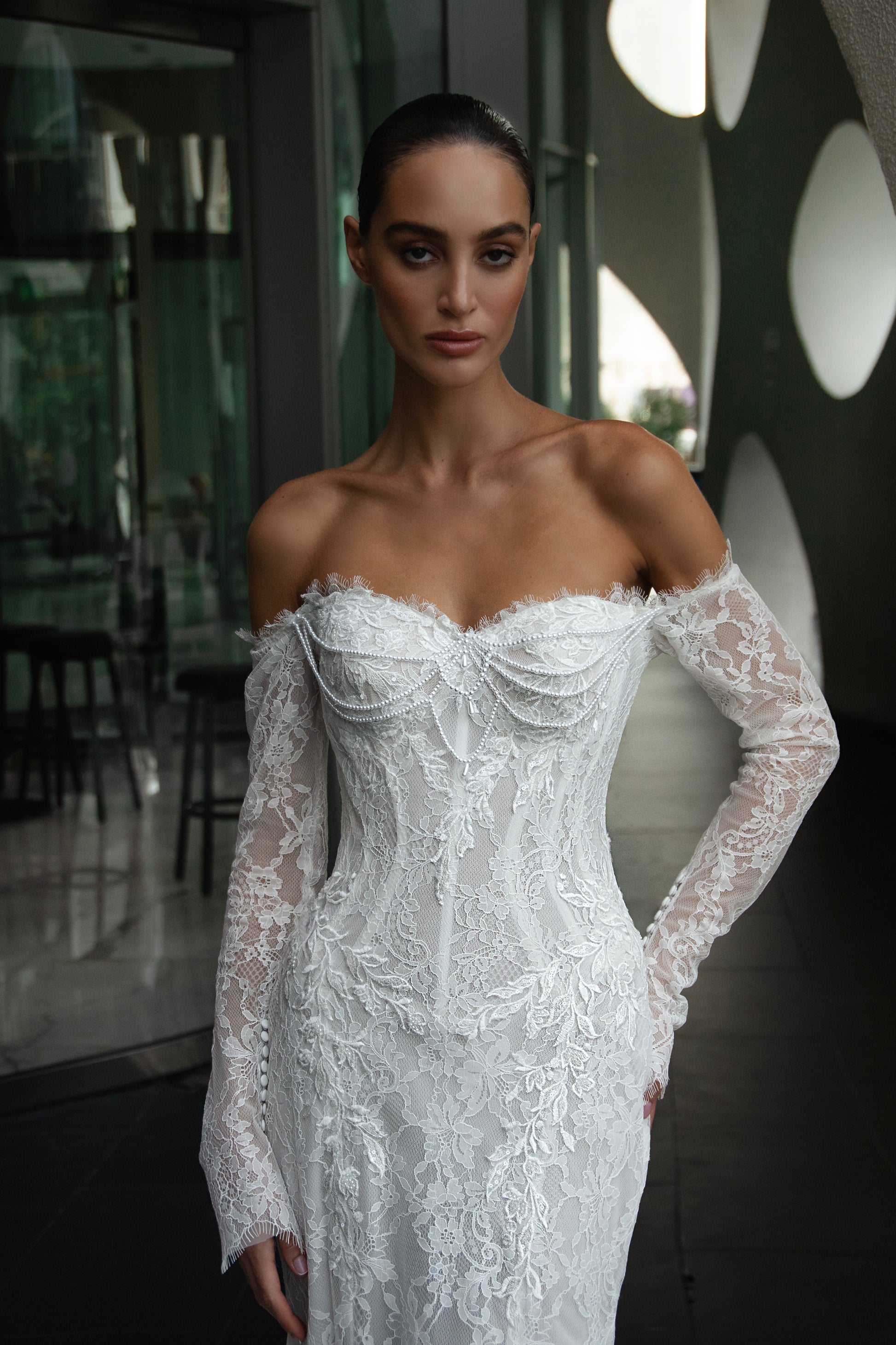 Off-shoulder lace wedding gown with long illusion sleeves, corset bodice, and chapel-length train.